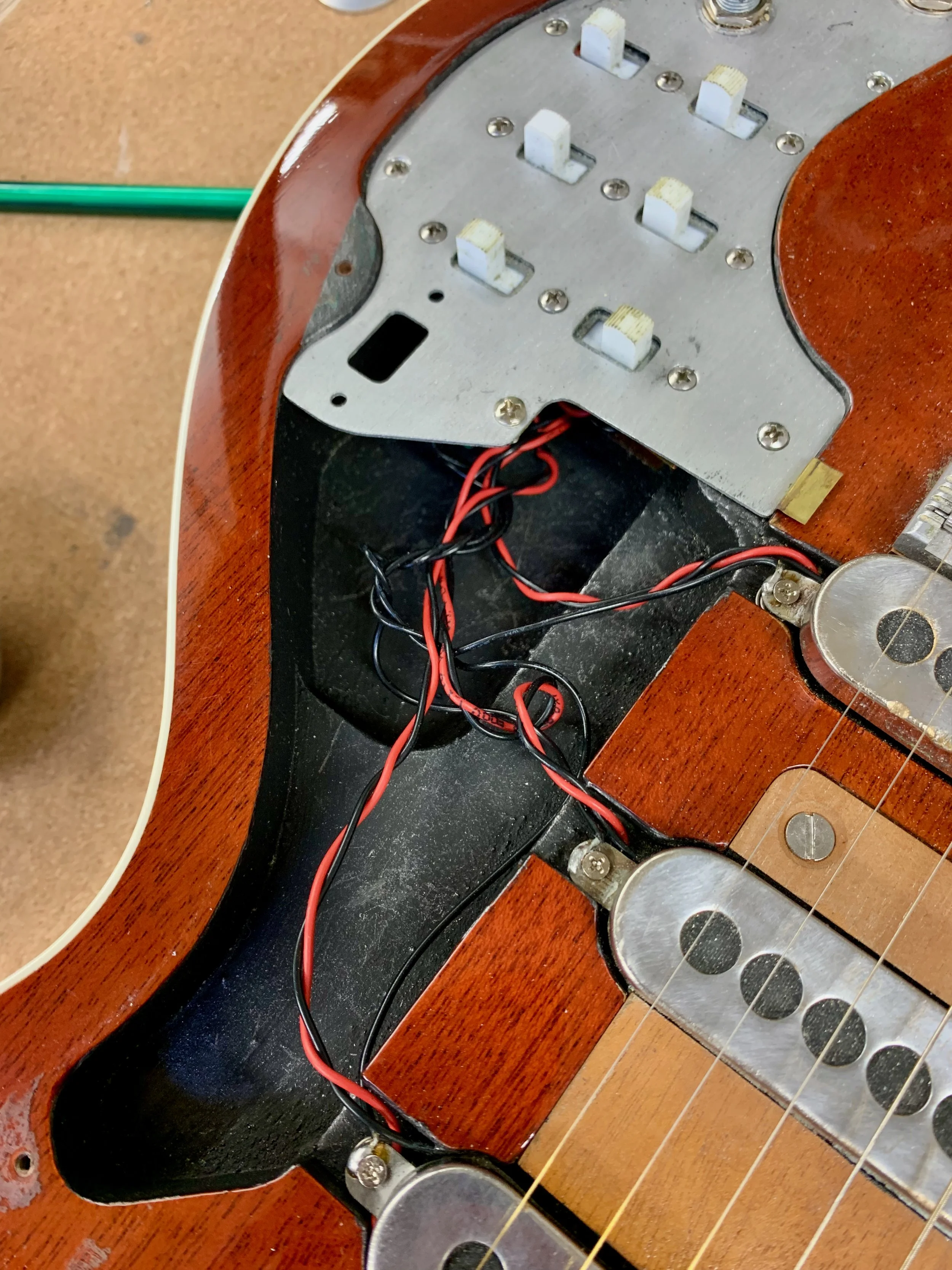 Een elektrische gitaar zonder snaren en bedraad, met de hals en body zichtbaar. De houten body is bruin en de metalen onderdelen, zoals de brug en schroeven, zijn zichtbaar.