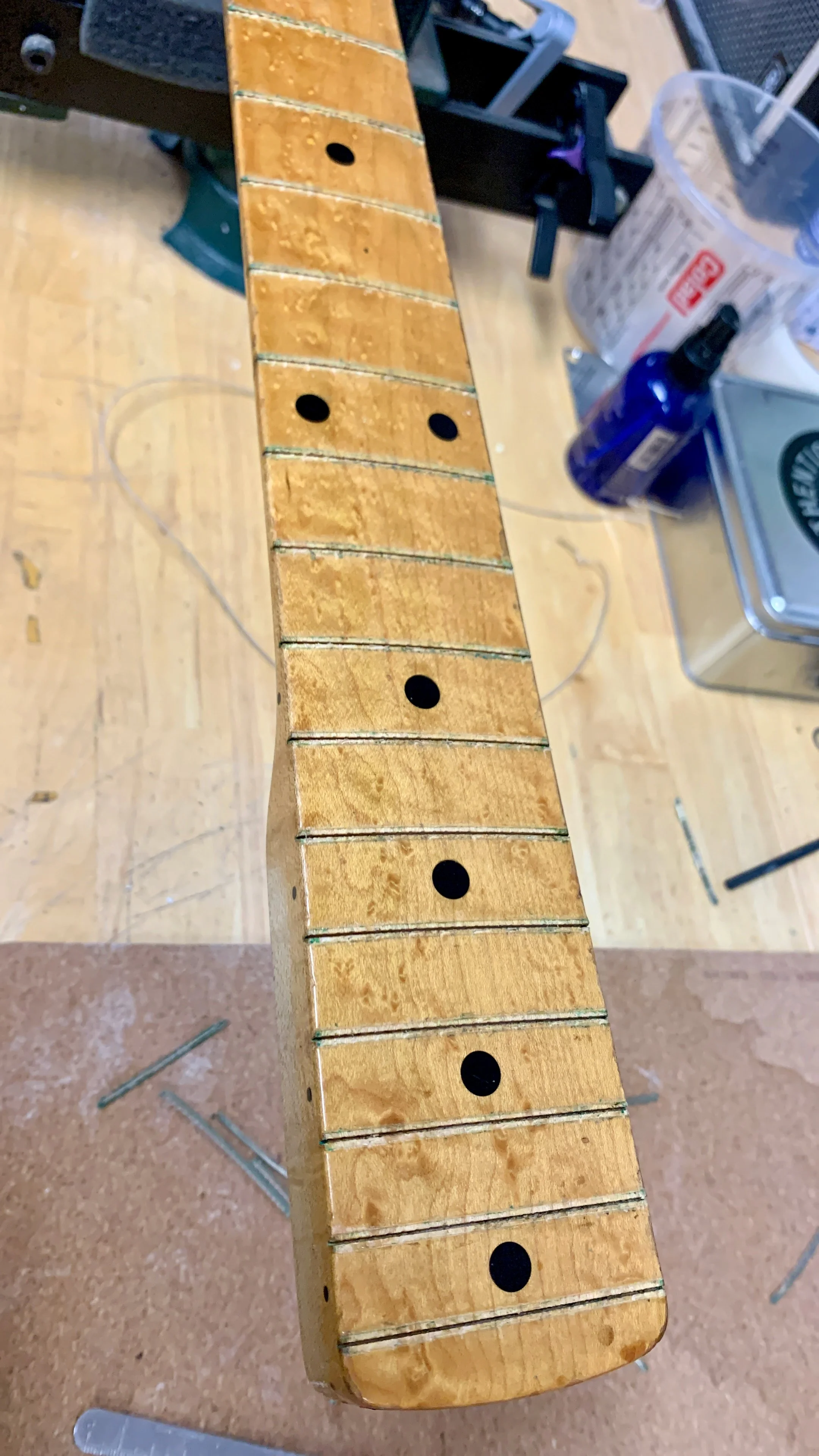 Een houten muziekinstrument, waarschijnlijk een xylofoon of marimba, in de maak, met zwarte vlekken op de houten balken en gereedschap en benodigdheden op een werktafel.