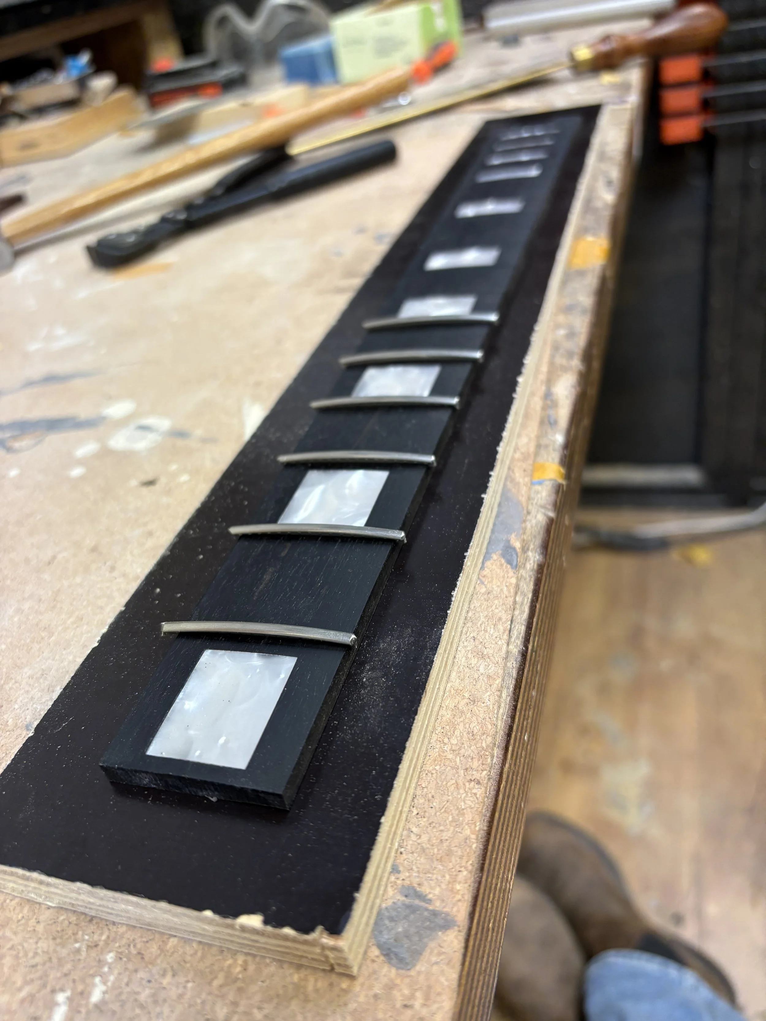 Een werkbank met een stuk hout dat een blackboard met metalen bevestigingen bevat, waarschijnlijk in een houtbewerking werkplaats.