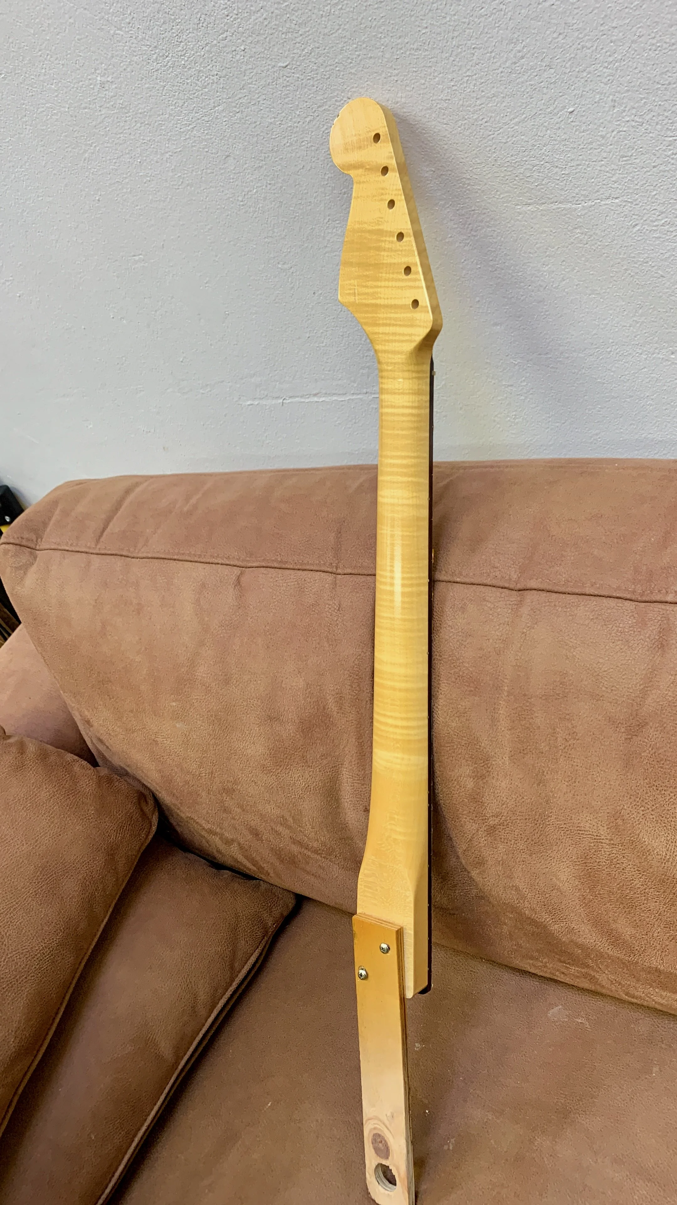 Geledeukte houten gitaakorpus zonder snaren, bovenaan tegen een witte muur.