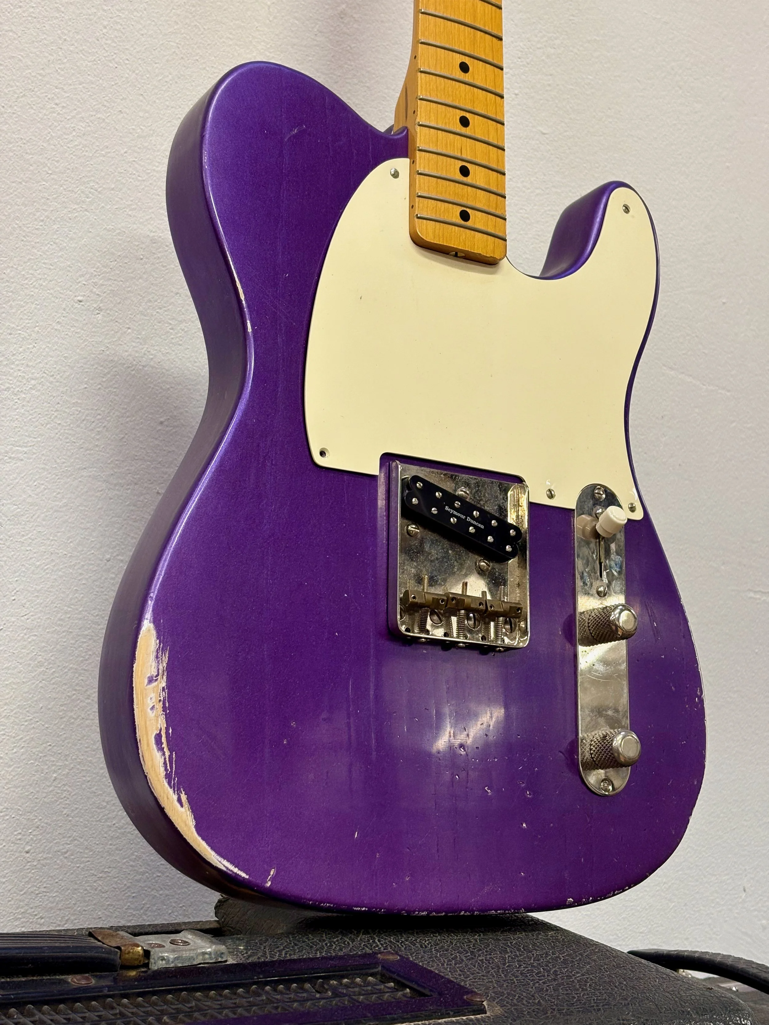 Een elektrische gitaar met een paarse body en een witte hals, zonder snaren, staand tegen een witte muur.