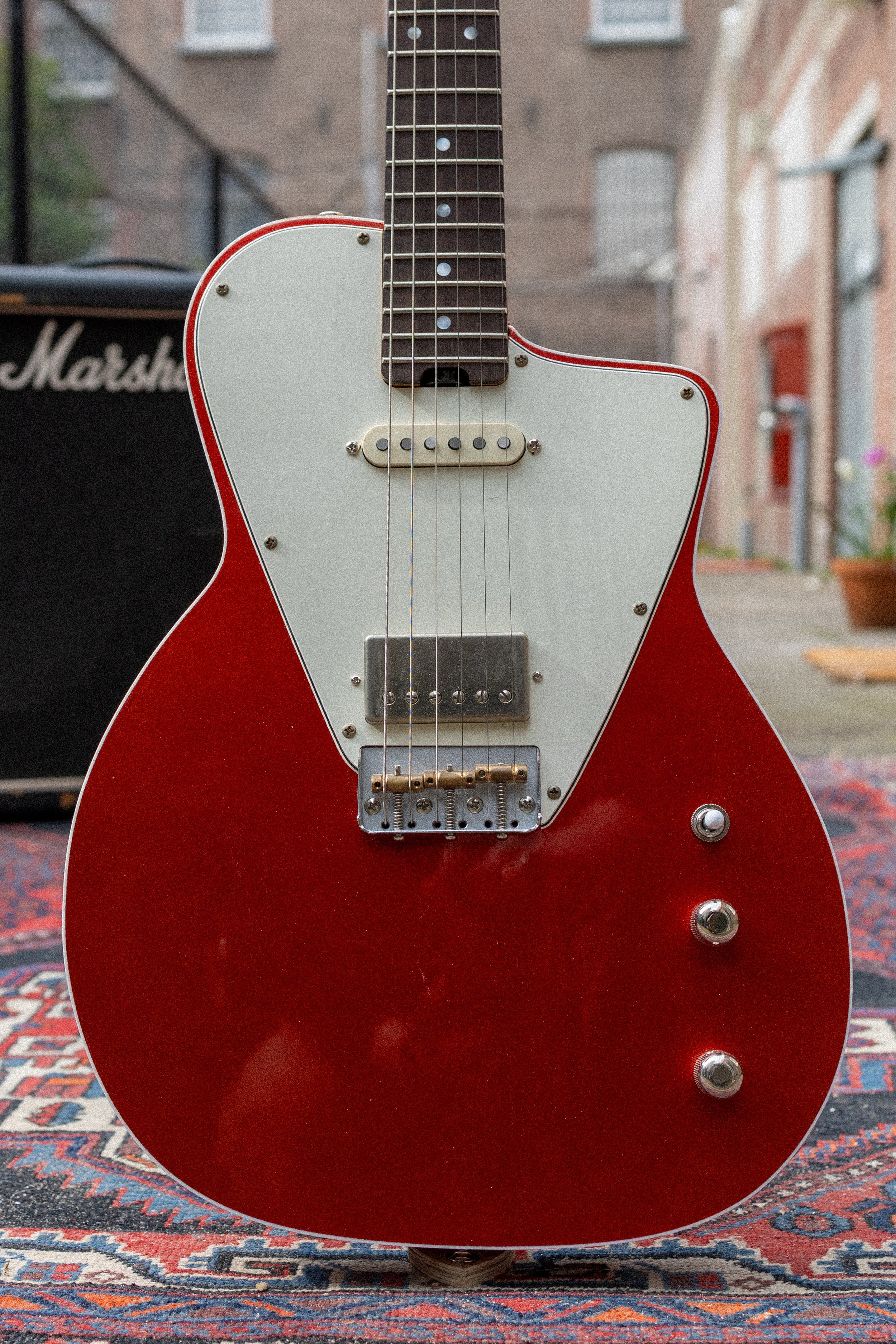 Close-up van een rode elektrische gitaar met wit-paarse witte body, op een tapijt met een patroon.