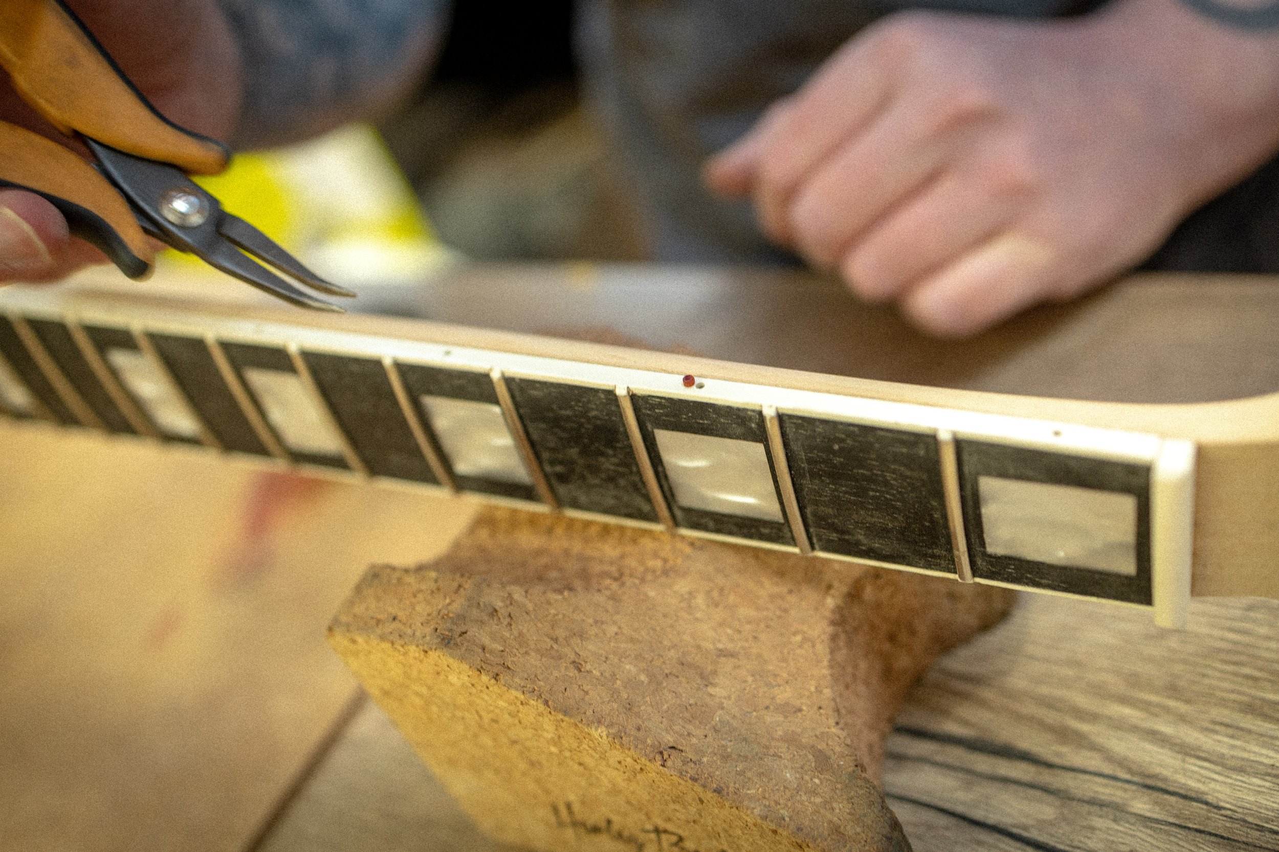 Hand met schaar snijdt een houten stuk dat gemarkeerd is met zwarte en witte vulkleur  op een werkbank.