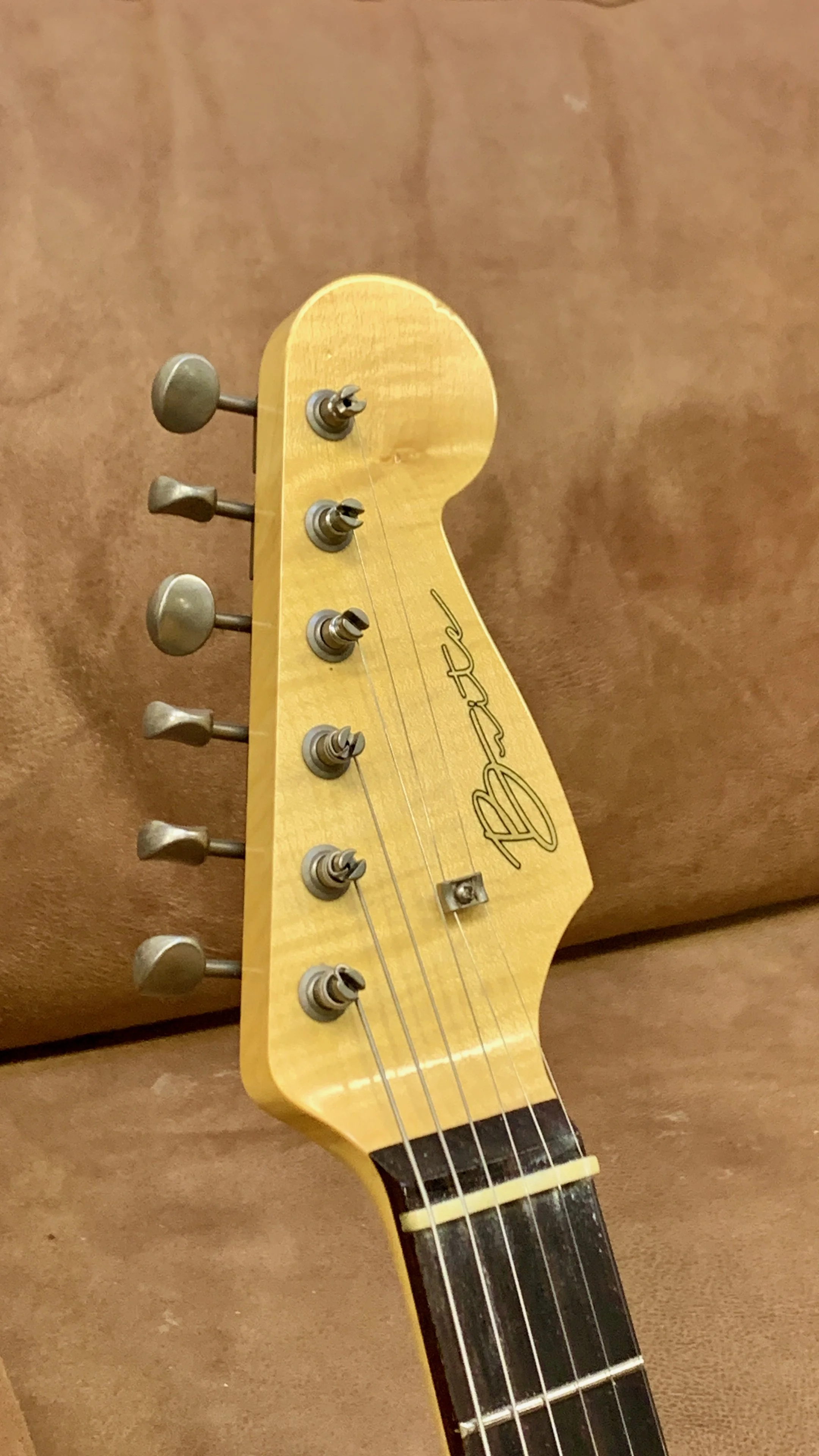 Close-up van het kopstuk van een Fender elektrische gitaar met zes tuning pegs en de naam 'Fender' op de kop.