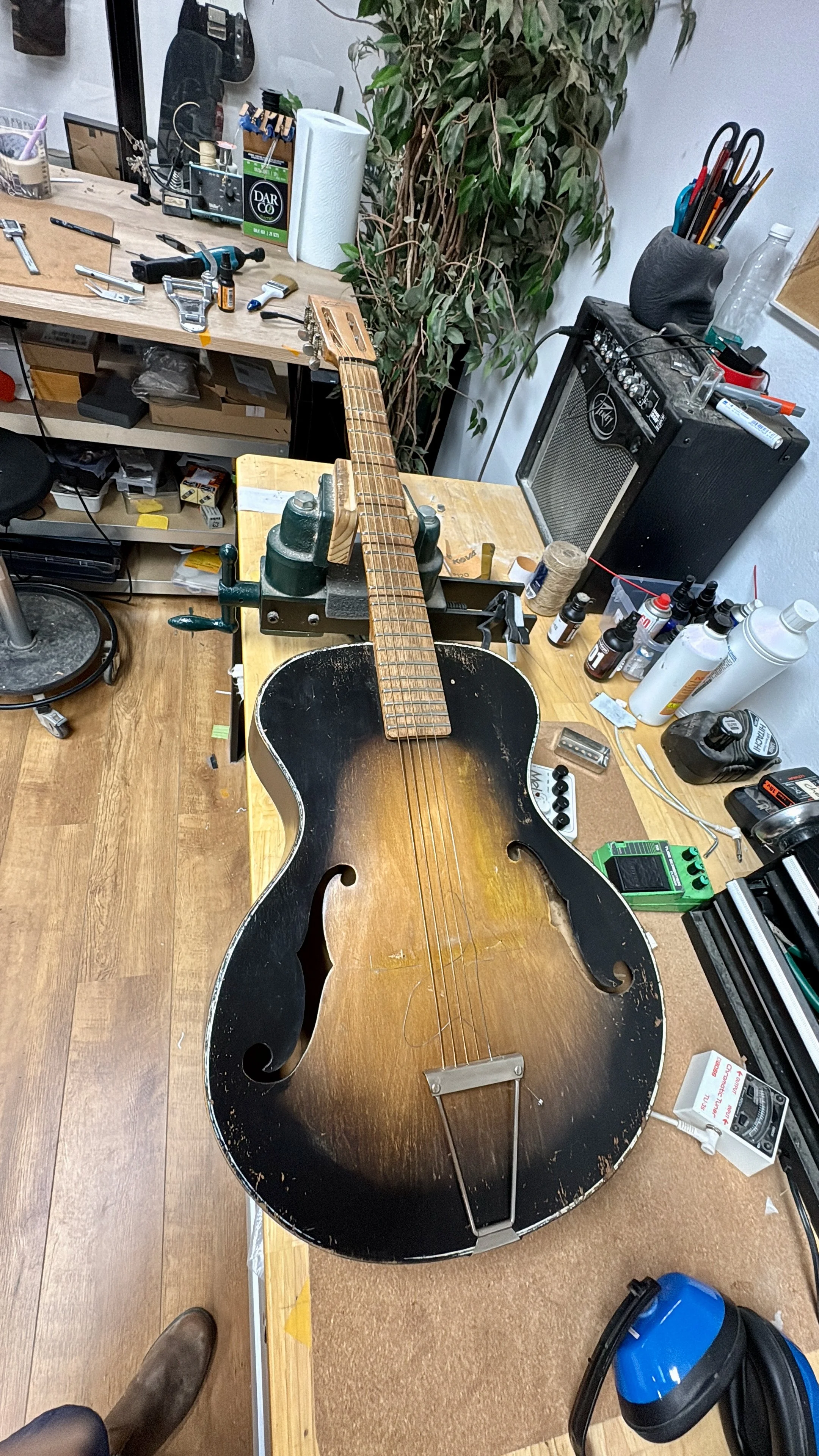 Een elektrische gitaar wordt gerepareerd of geassembleerd in een werkplaats met diverse gereedschappen en onderdelen op een werkbank.