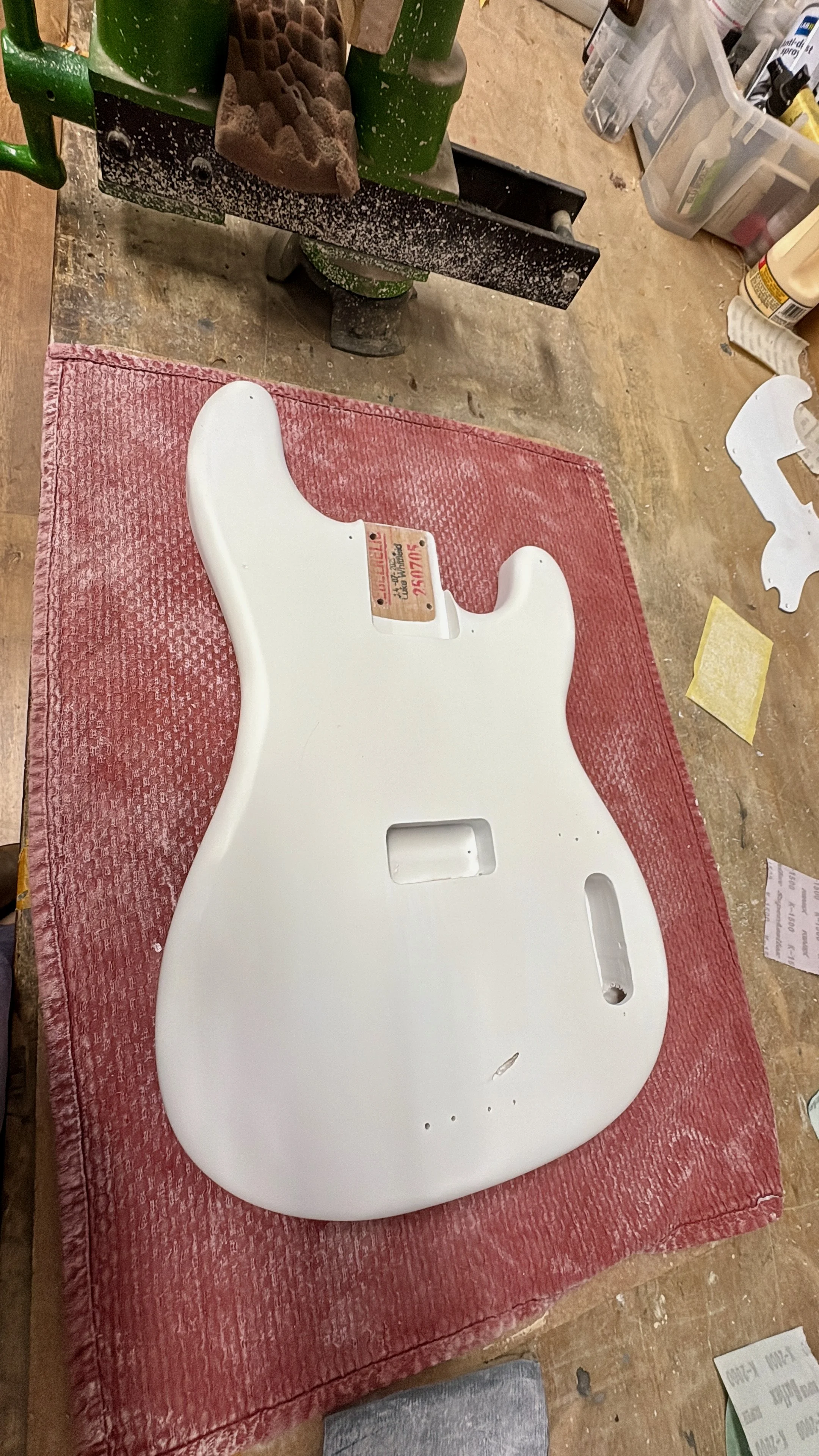 Een witte elektrische gitaarkast op een rode mat in een werkplaats.