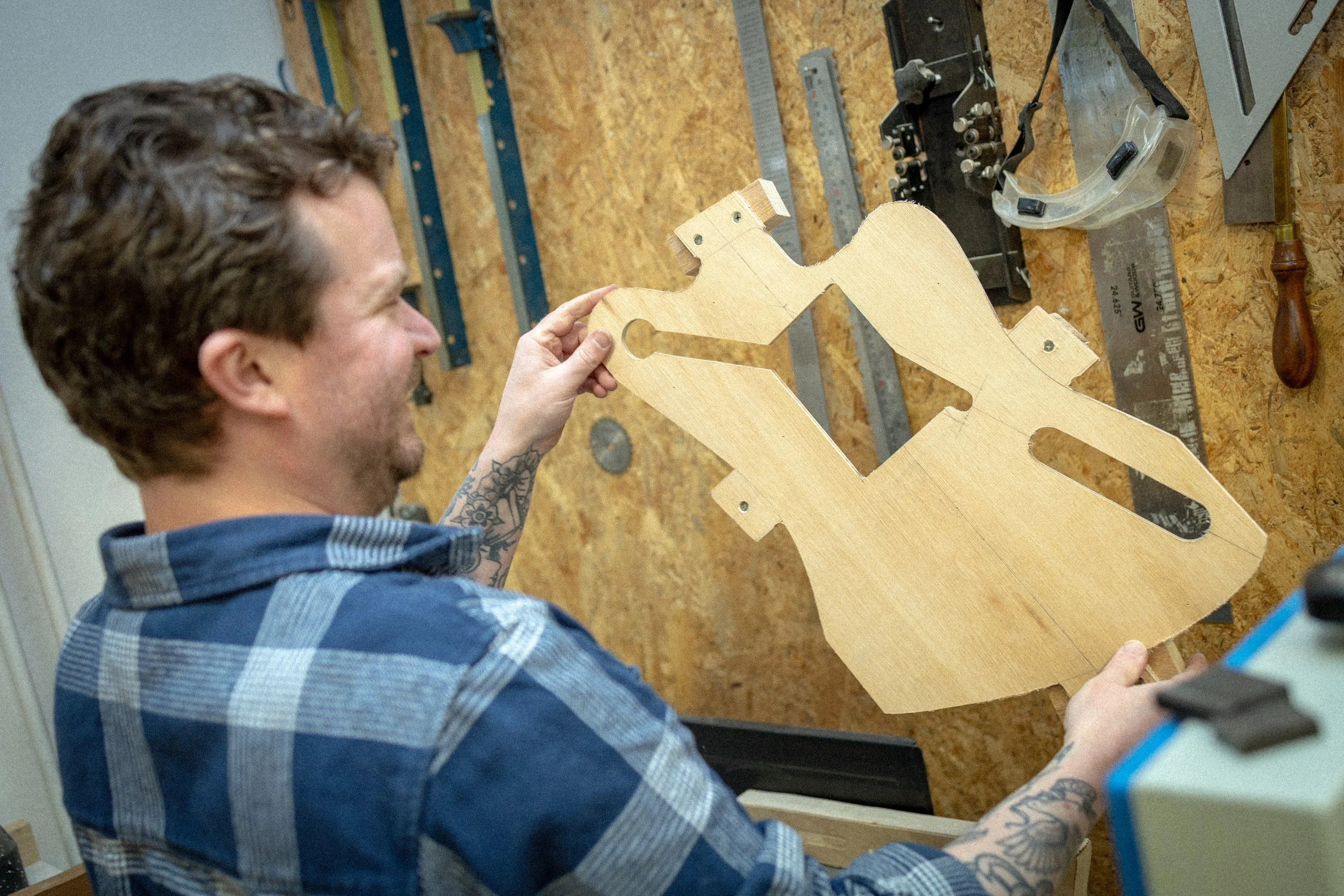 Man houdt een houten gitaarvasthouden en werkt aan het maken, in een werkplaats met gereedschap op de muur