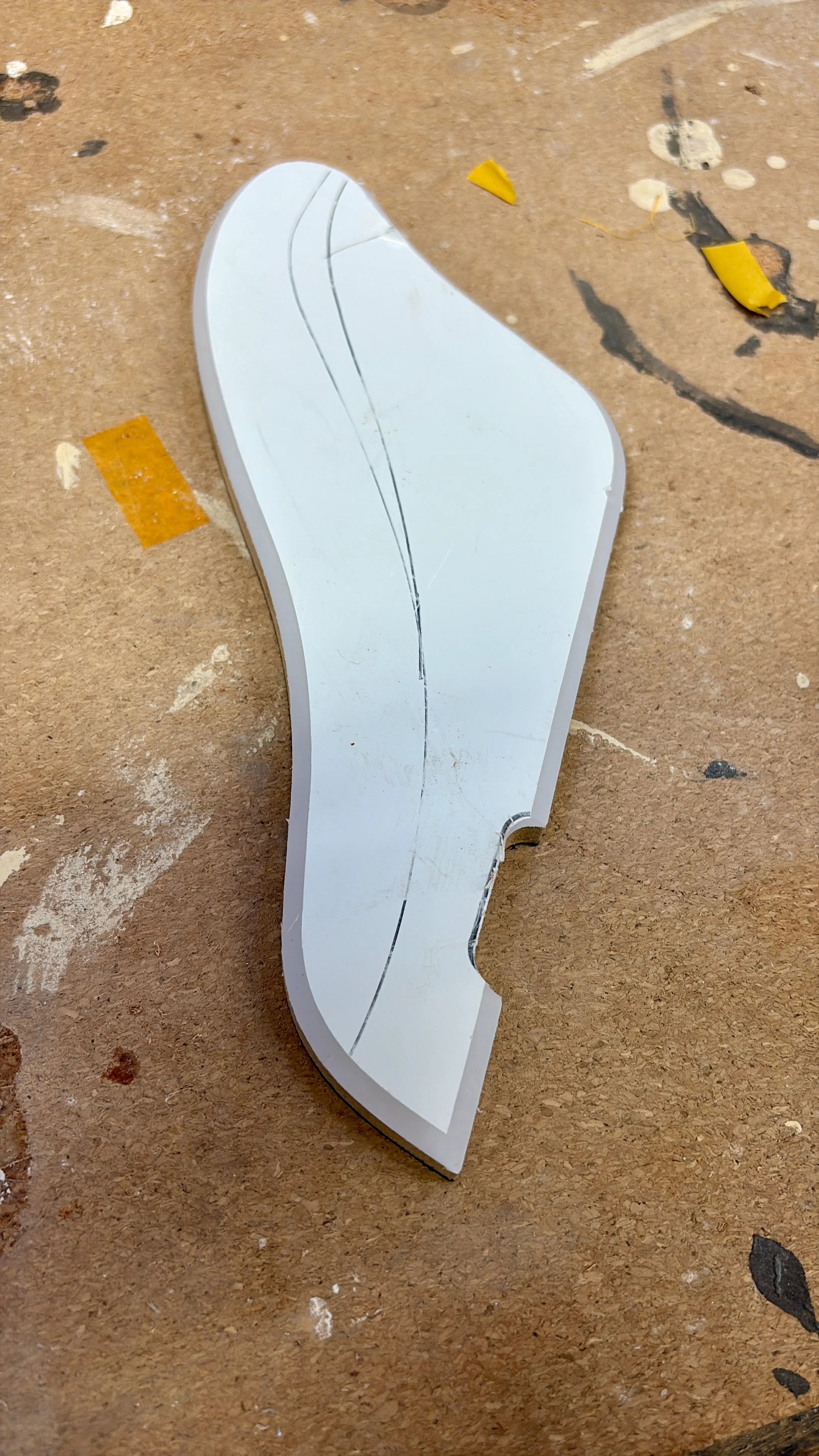 Een gebroken wit plastic schaaltje op een stoffige werktafel met verfspatten en stukjes tape.