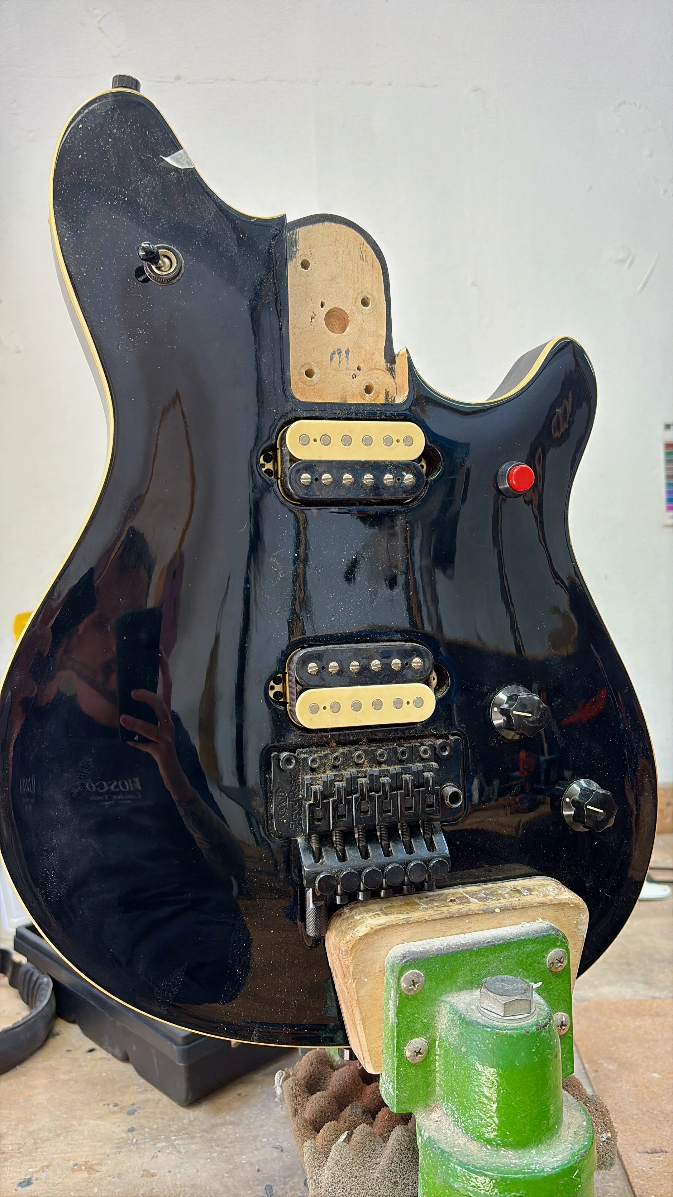 De afbeelding toont een elektrische gitaar in reparatie of in elkaar zetten, zonder snaren en met zichtbare elektronica en magneten.