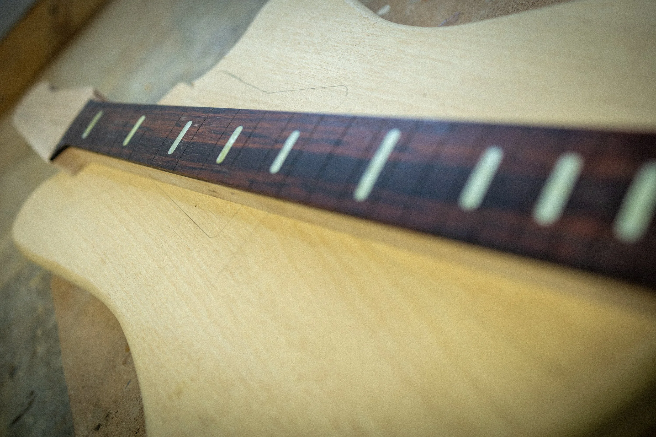 Close-up van een gitaarhals met fret markers en snaren, rustend op een houten oppervlak.