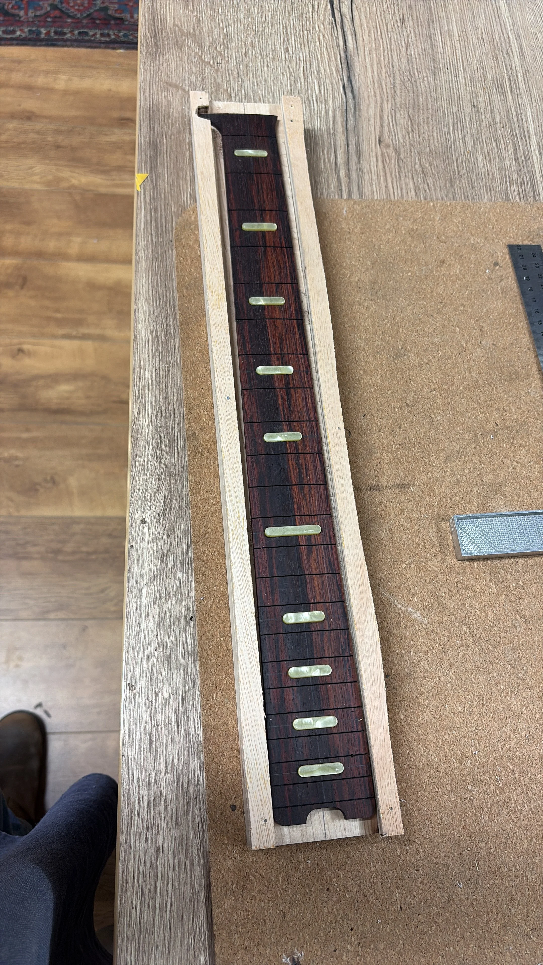  een werkbank met een lang stuk van een gitaarhals met fretboard en fret markers