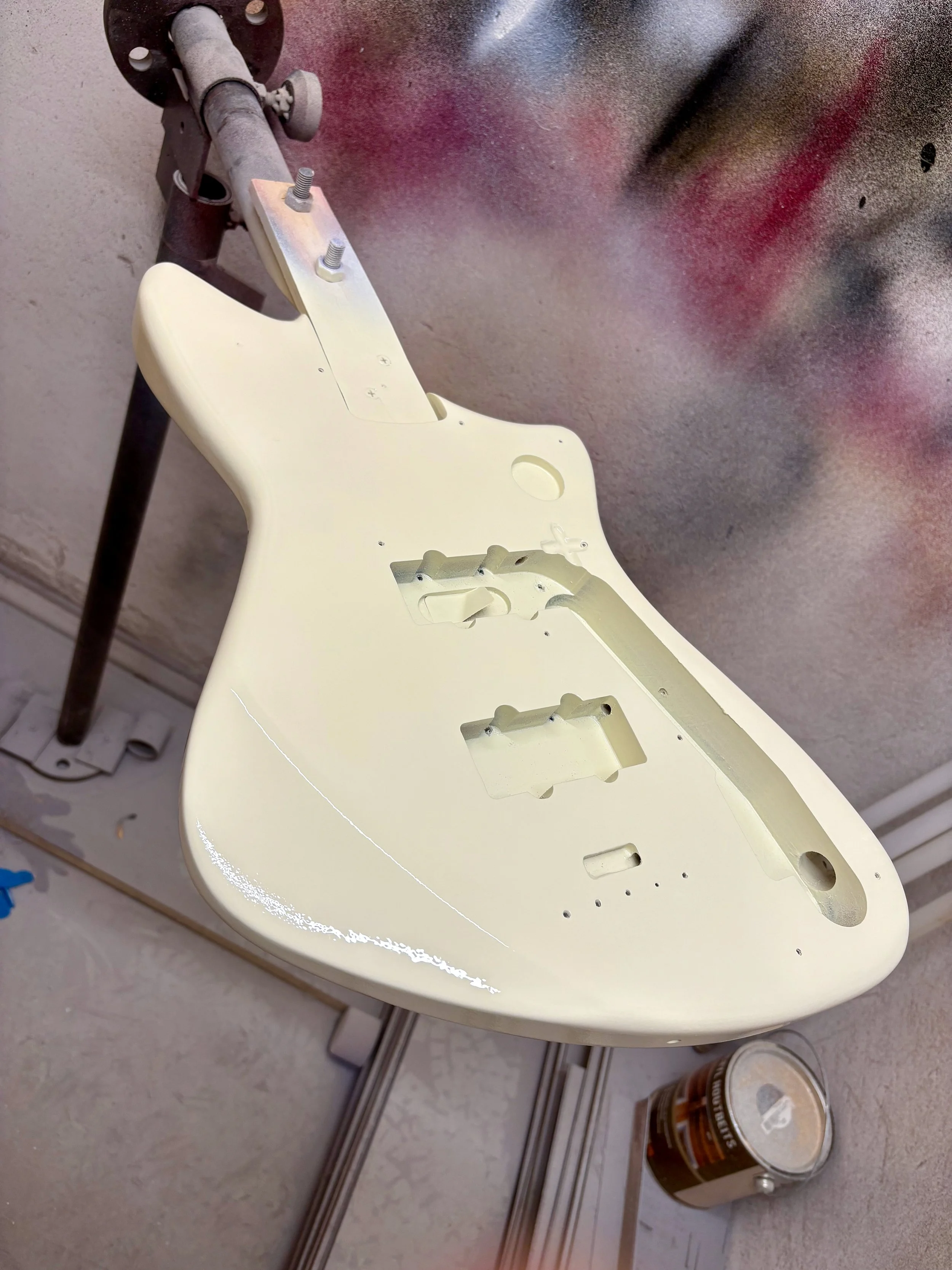 Een witte gitaarkast ligt op een tafel, er is verf en gereedschap aanwezig, mogelijk in een werkplaats.