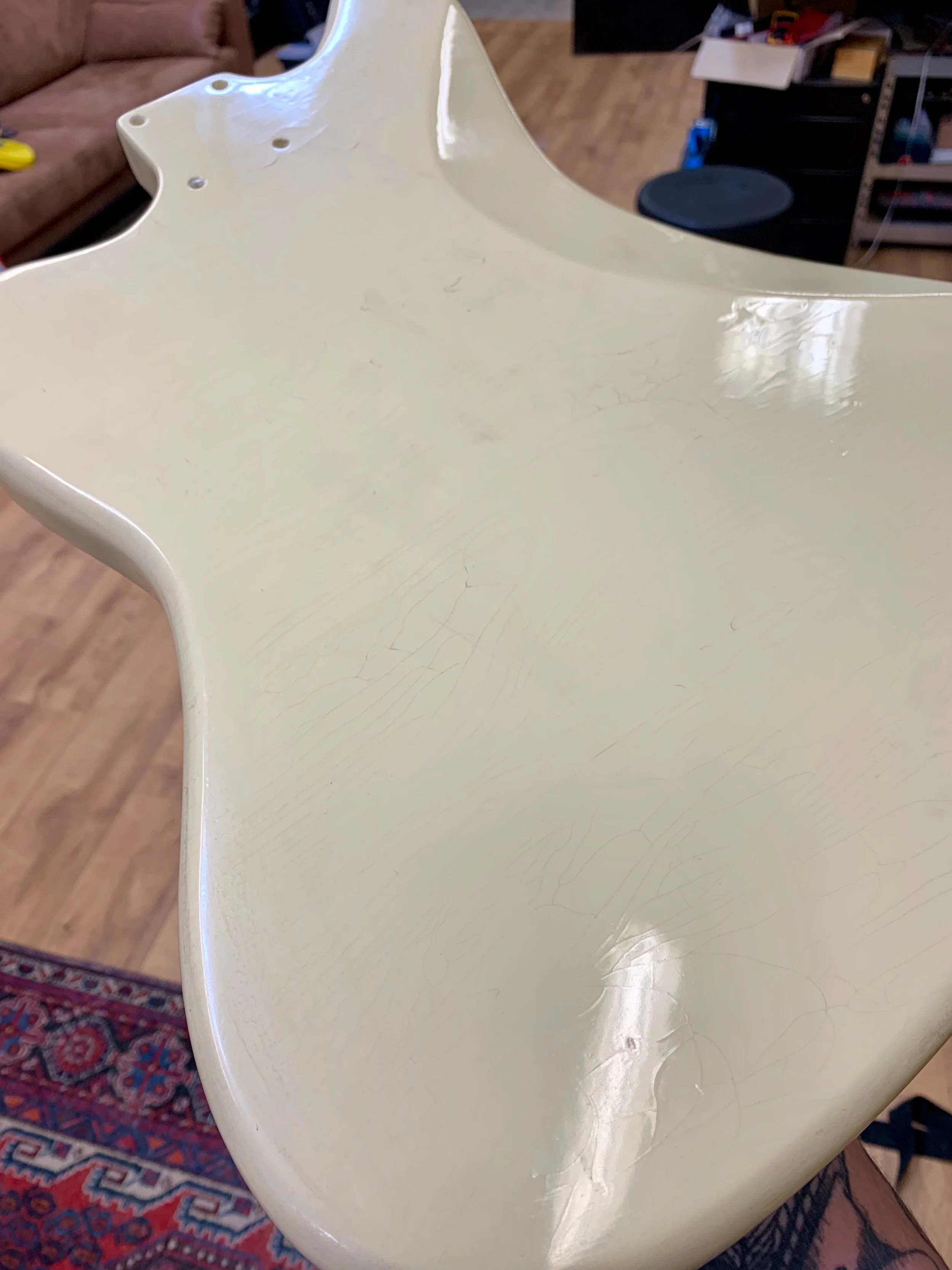 Een witte houten tafel met duidelijke krassen en slijtageplekken, in een woonkamer met een tapijt en meubels op de achtergrond.