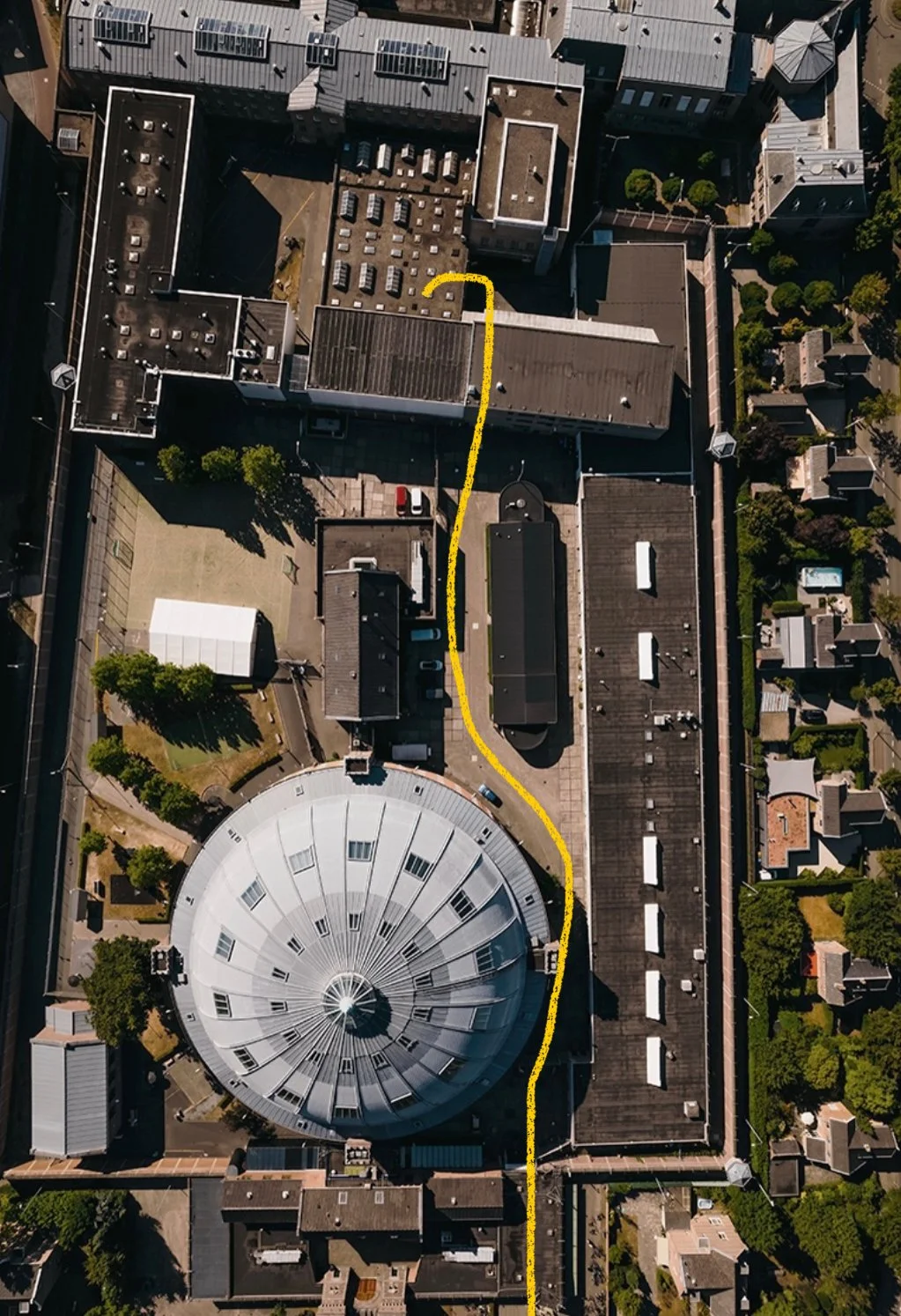 Hoogwaardige luchtfoto van een stadscentrum met een grote, ronde, metalen koepel en verschillende gebouwen, met een gele lijn die een pad aangeeft.