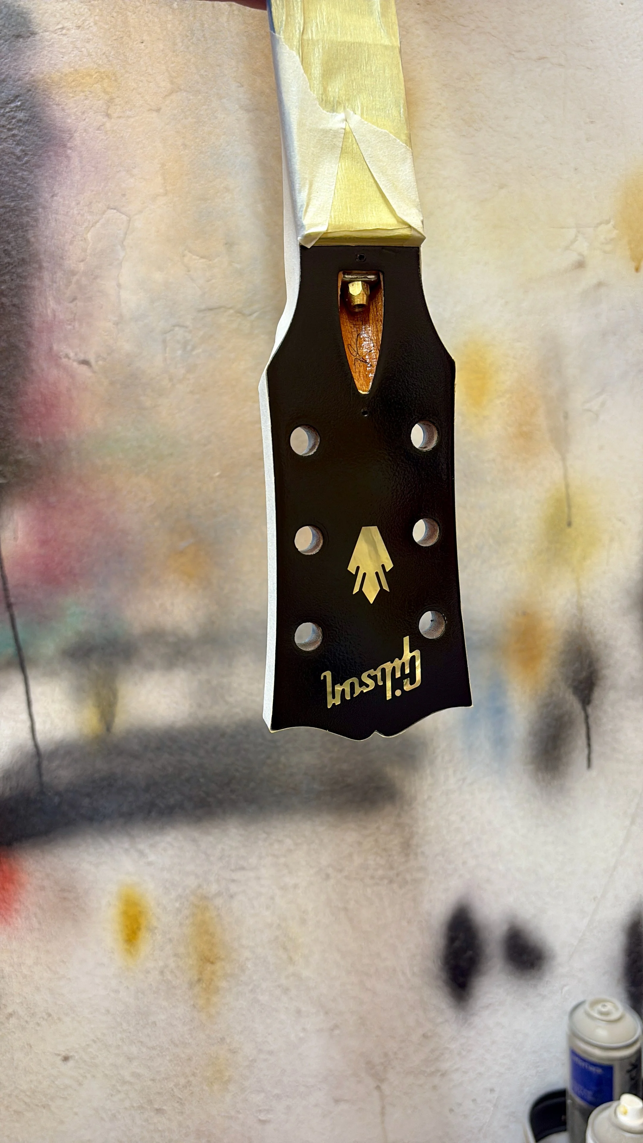 Close-up van een zwarte schildermes met een houten handvat, bevestigd aan een muur dat deels afgeplakt en geschilderd is in een atelier of verfruimte.