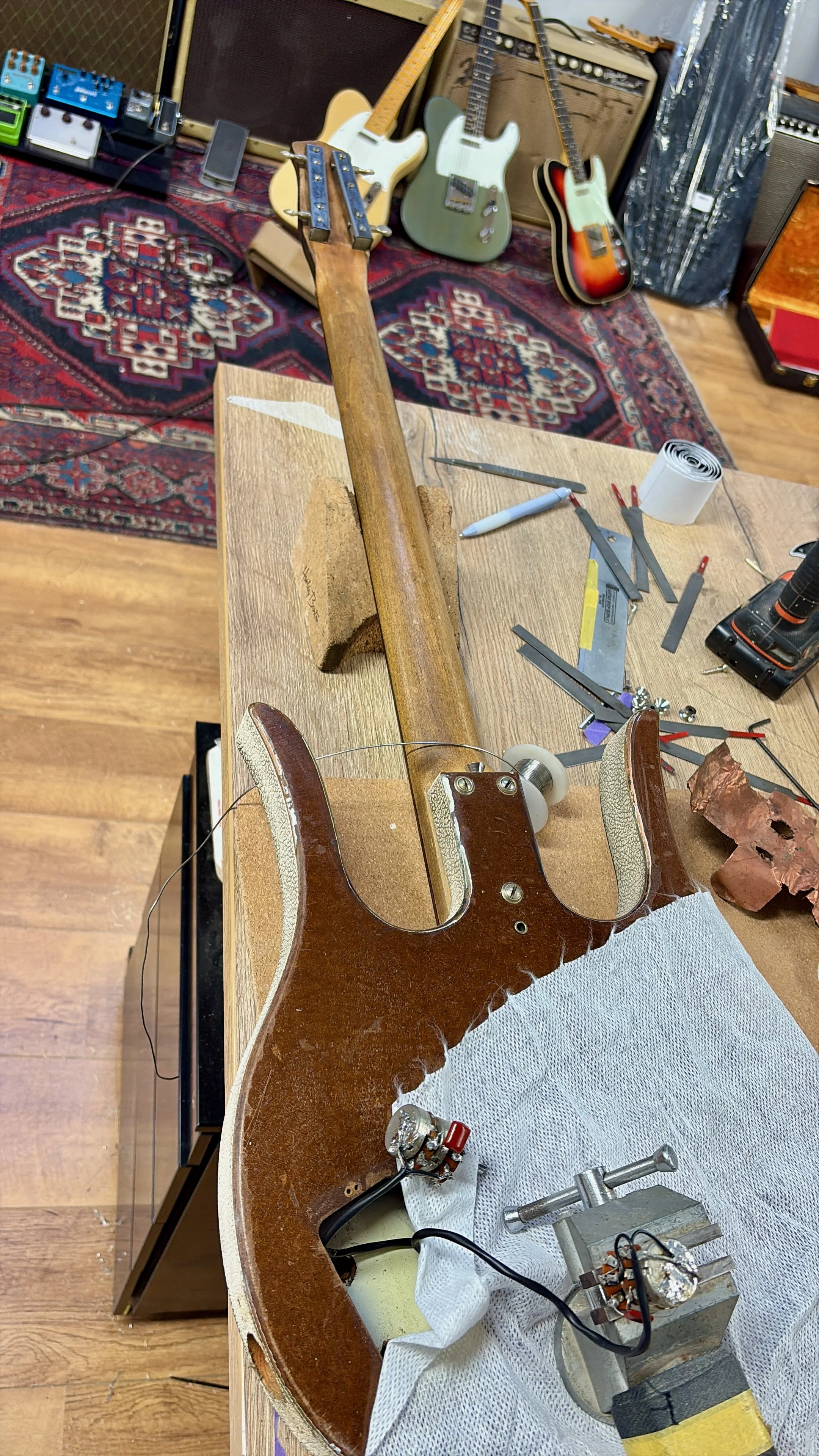 Binnenkant van een elektrische gitaar onder reparatie op een werkbank, met gereedschap en onderdelen rondom.