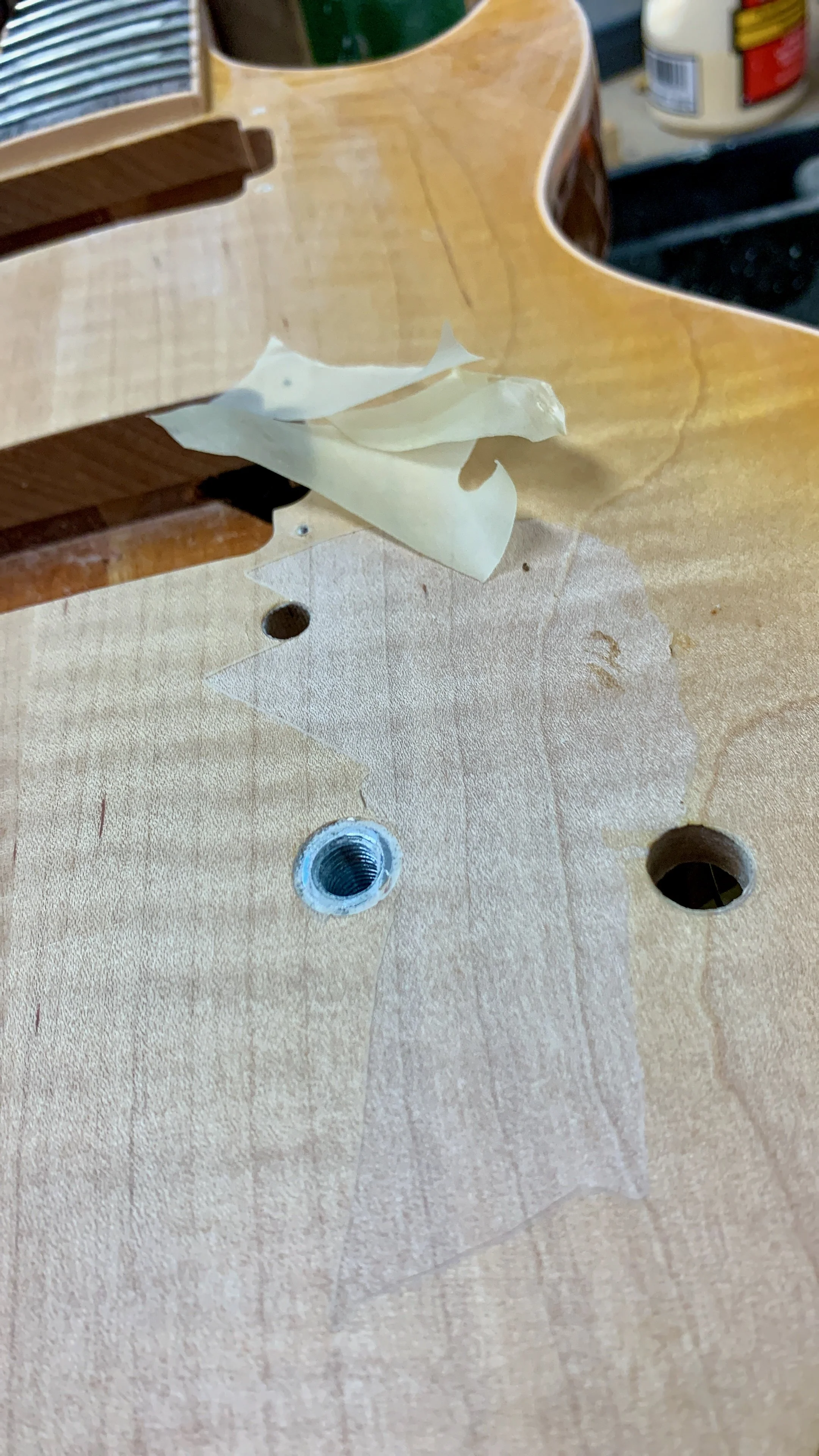 Een houten werkbank met een stuk papier, een schroefgat en een uitsparing, mogelijk voor een apparaat of component. Op de achtergrond staan dozen of containers.