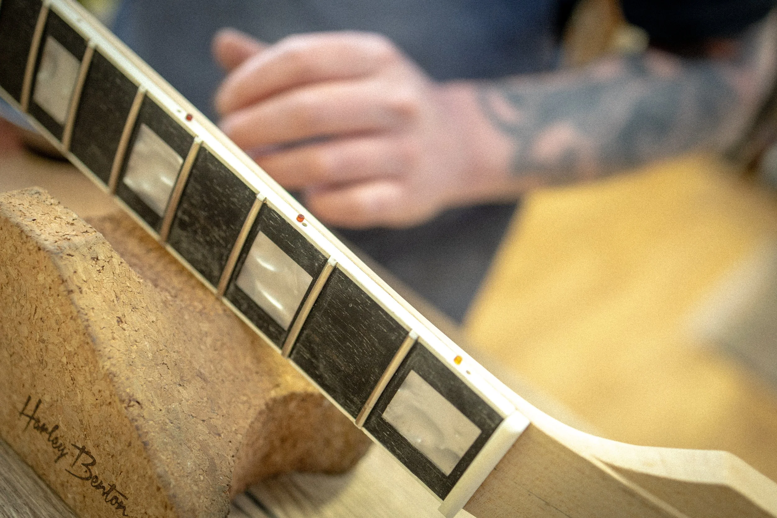 Close-up van een gitaarhals met frets en fretmarkers, met een vinger die klaar is om te spelen.