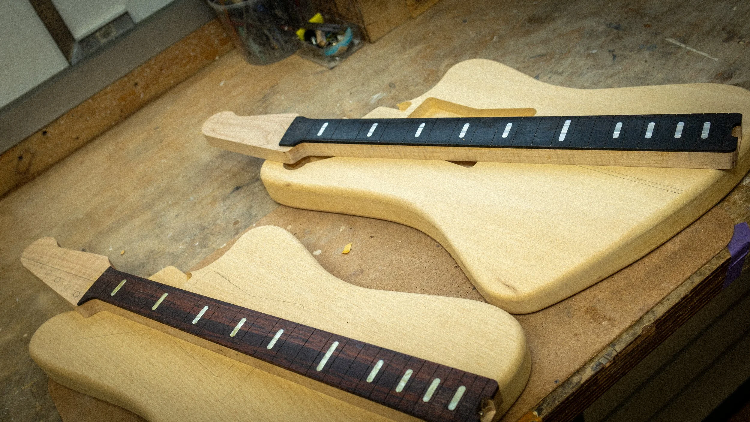 Afbeelding van een werkbanken met onvoltooide houten elektrische gitaar kaders, met fretborden en lichaam vormen, in houtbewerkingswerkplaats.