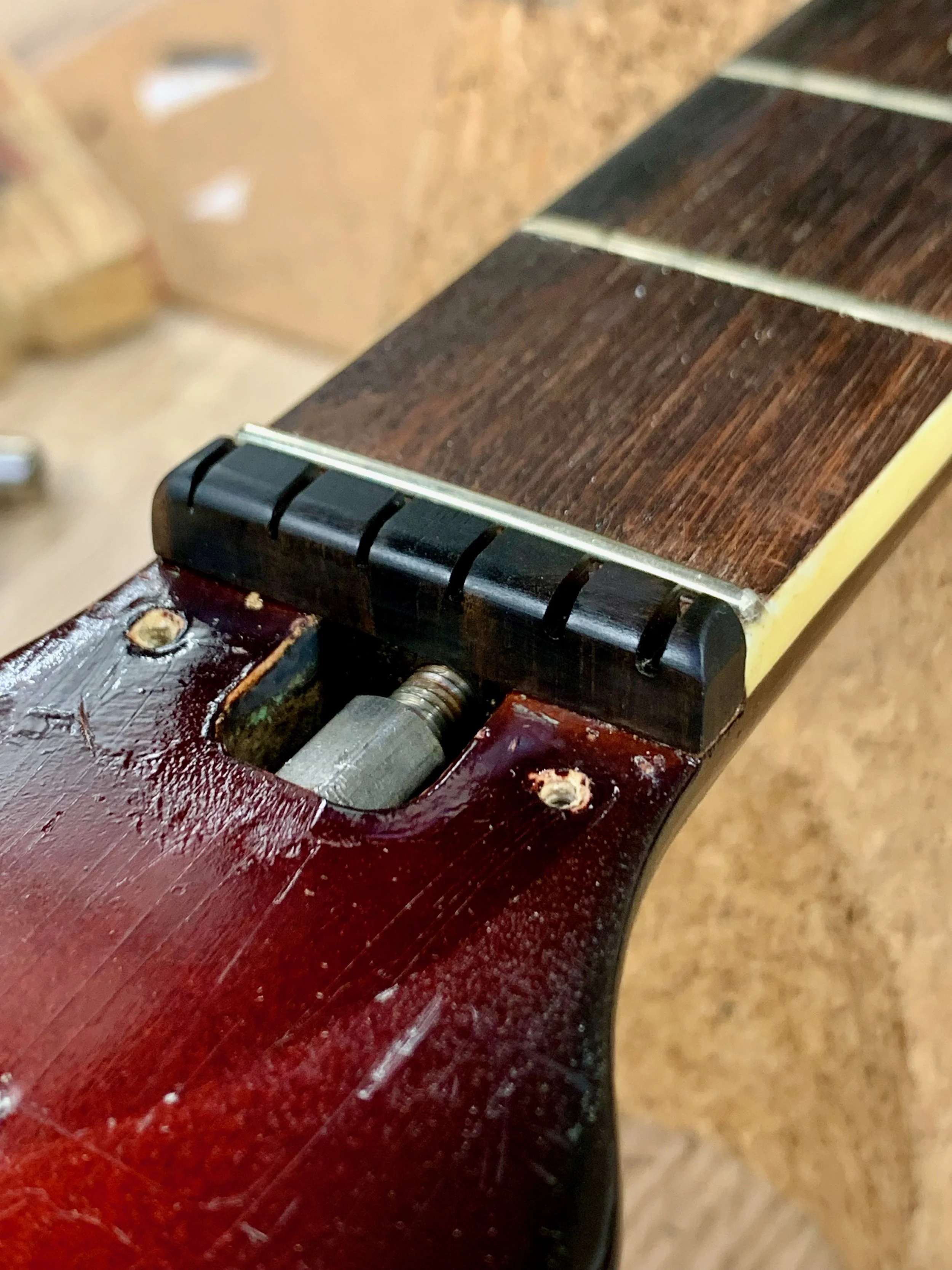 Close-up van een houten muziekinstrument, mogelijk een gitaar, met een beschadigd en gekleurde hals en enkele gescheurde snaren.