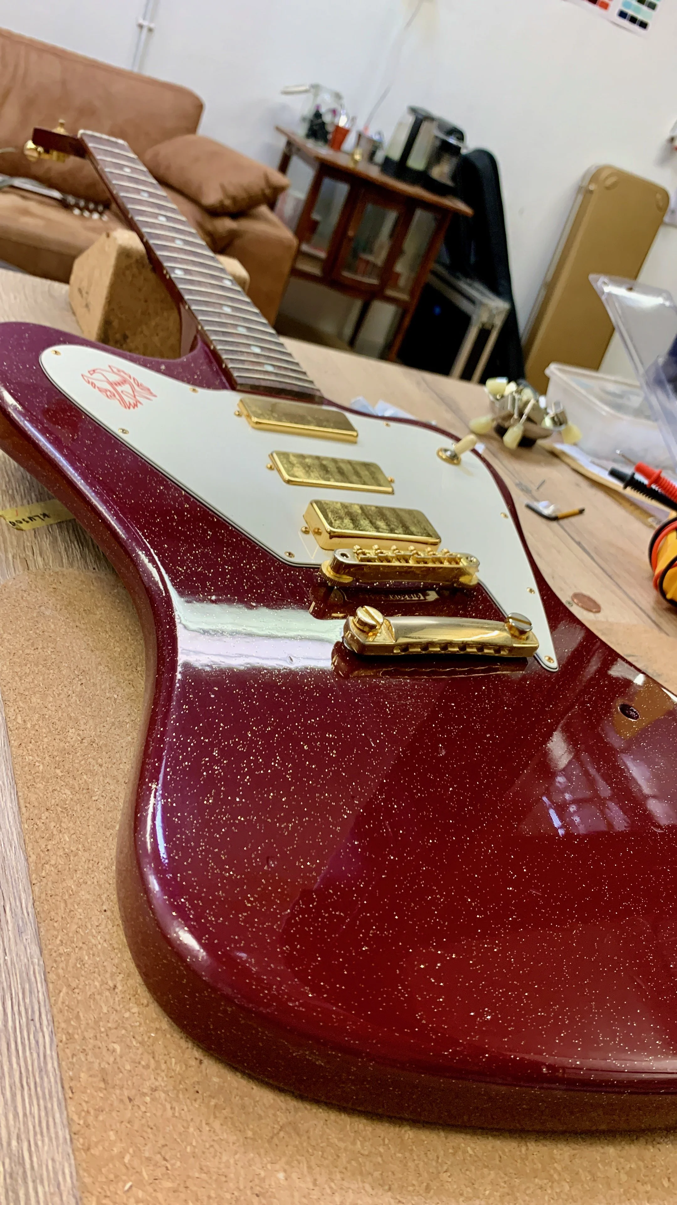 Een rode, glanzende elektrische gitaar met goudkleurige hardware ligt op een werktafel in een soort werkplaats of reparatieruimte.