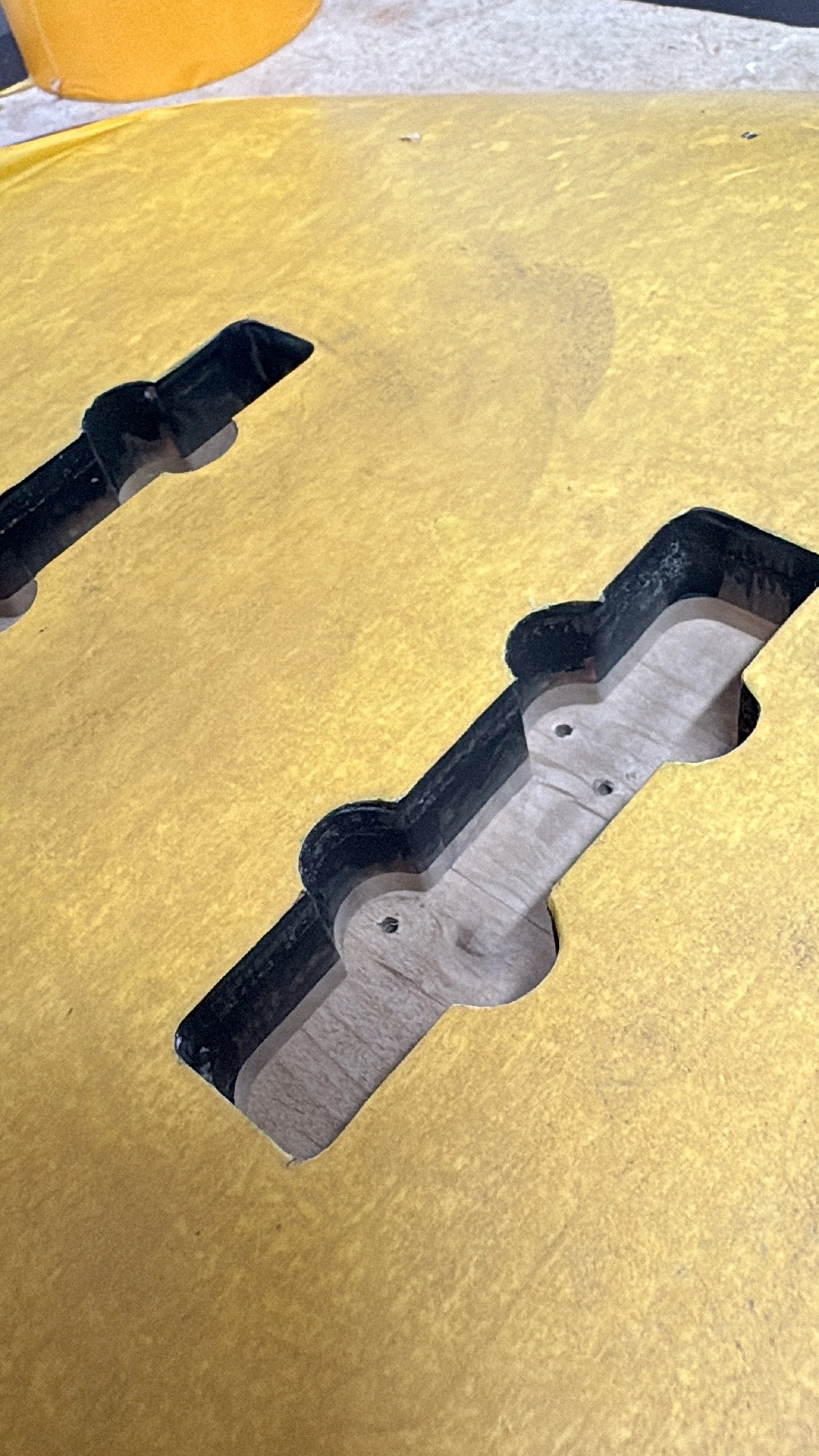 Een tafel met een opening waarin een houten onderstel zichtbaar is, een stuk van een zwarte hoek en een gele tafelblad met uitsparingen.