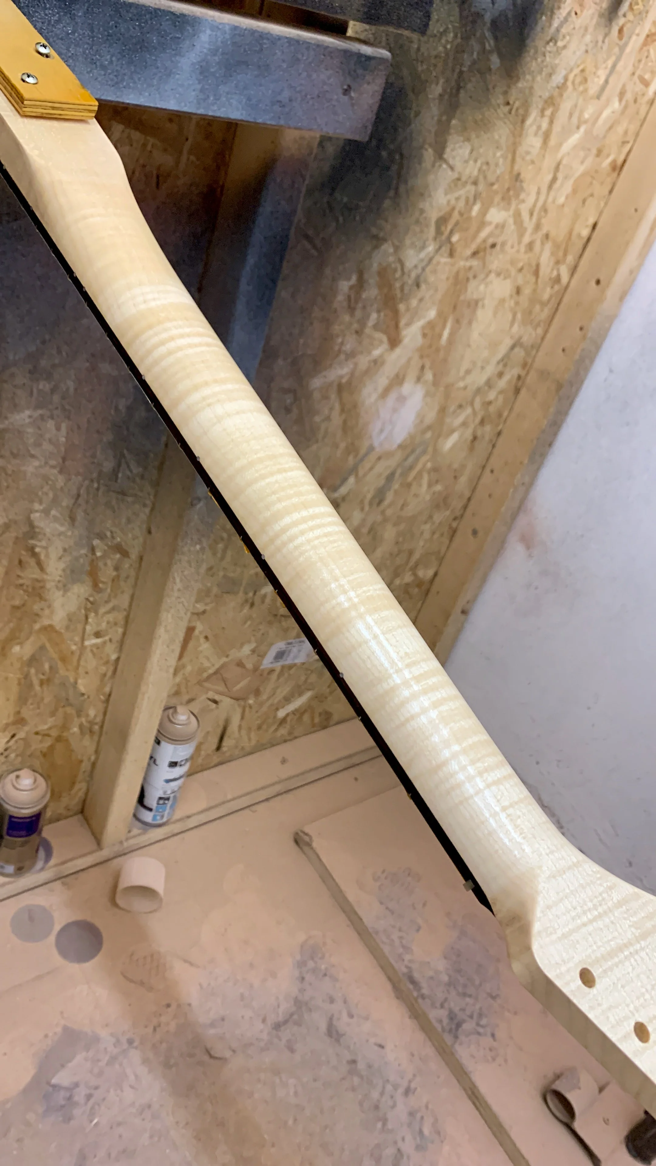 Een bouwplaats met multiplex platen, verfspuitbussen, stukjes tape en een lange rol behangpapier op de vloer.