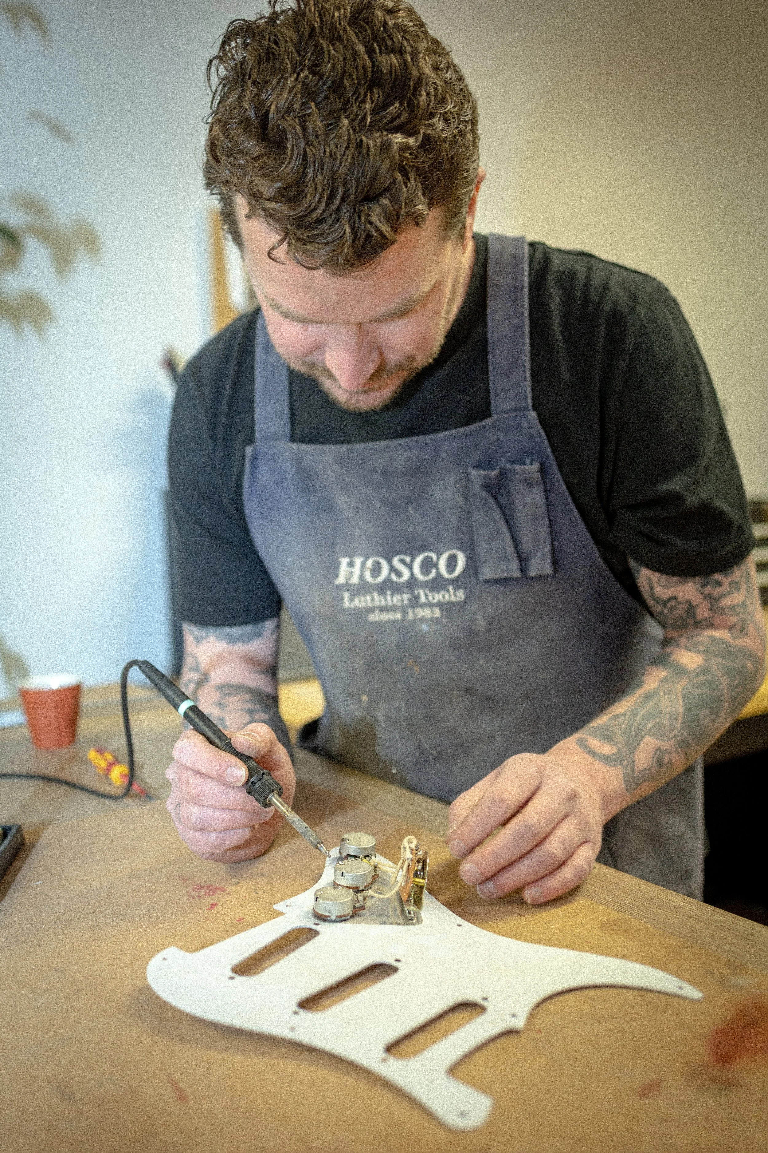 Man die een elektrische component soldeert op een houten tafel met een stuk houten plank en een witte componentenhouder.