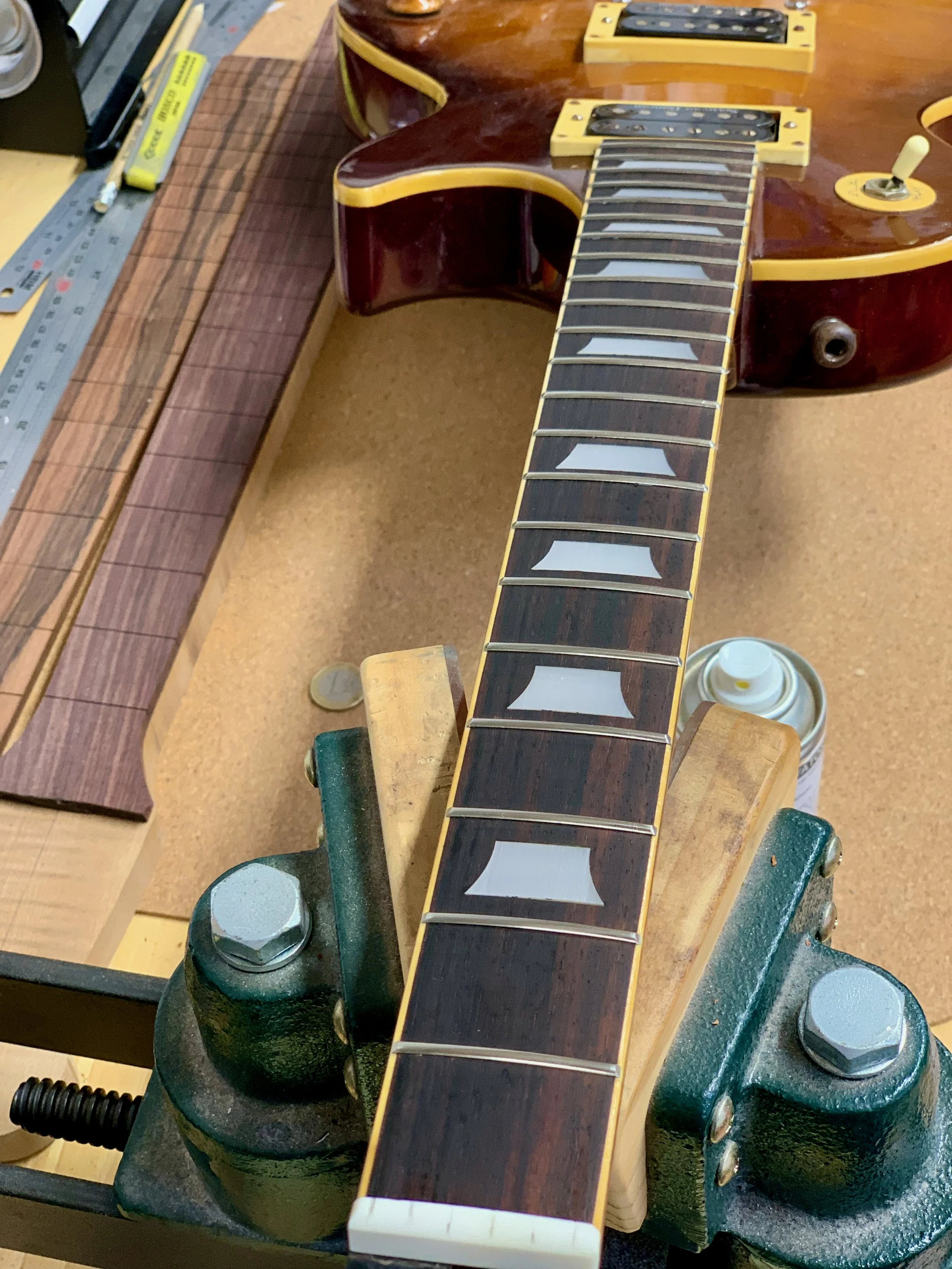 Een elektrische gitaar ligt op een werkbank met gereedschap en een houtblok.