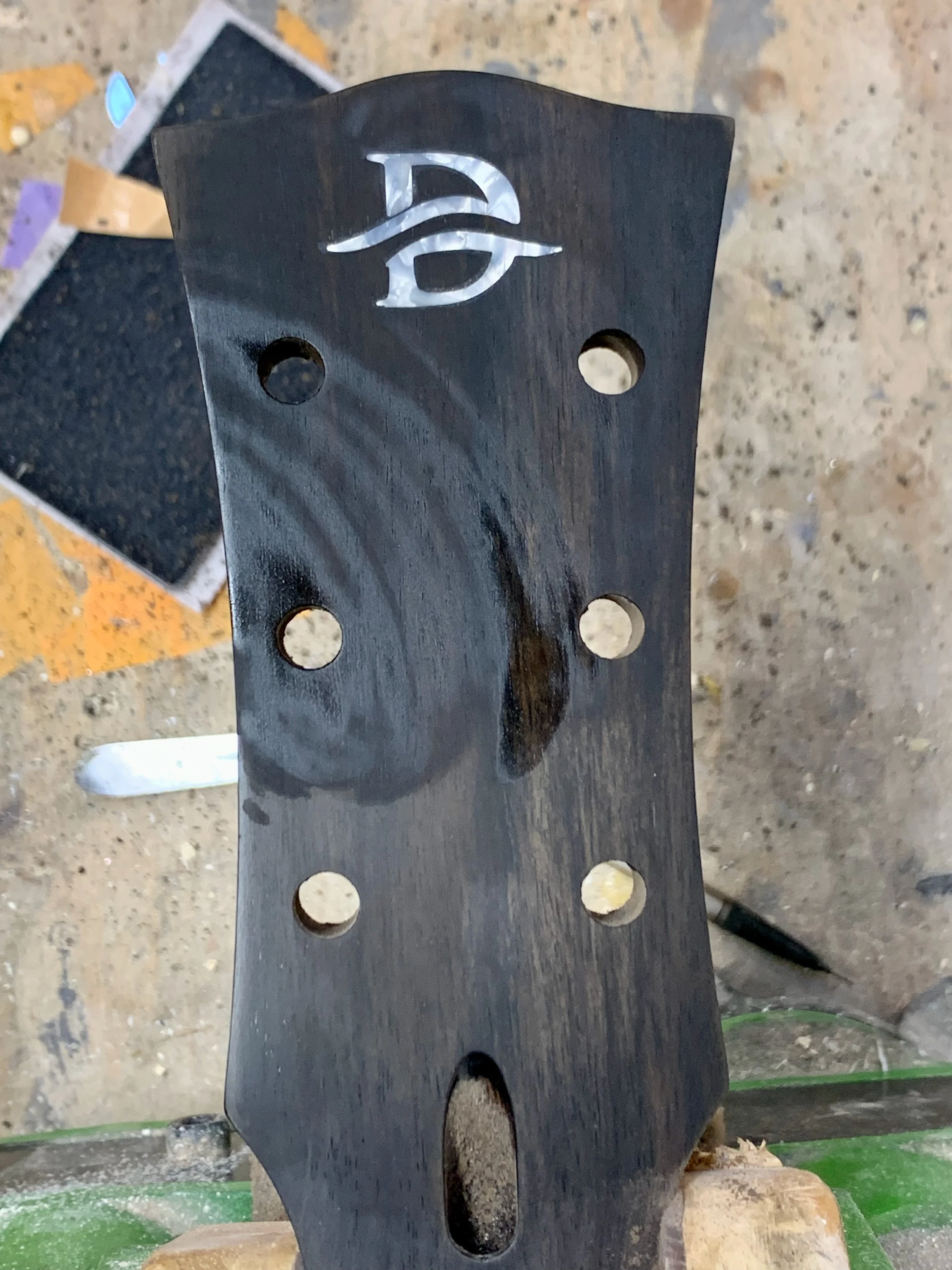 Zwarte houten snijplank met een merkteken en meerdere gaten, op een werkbank.