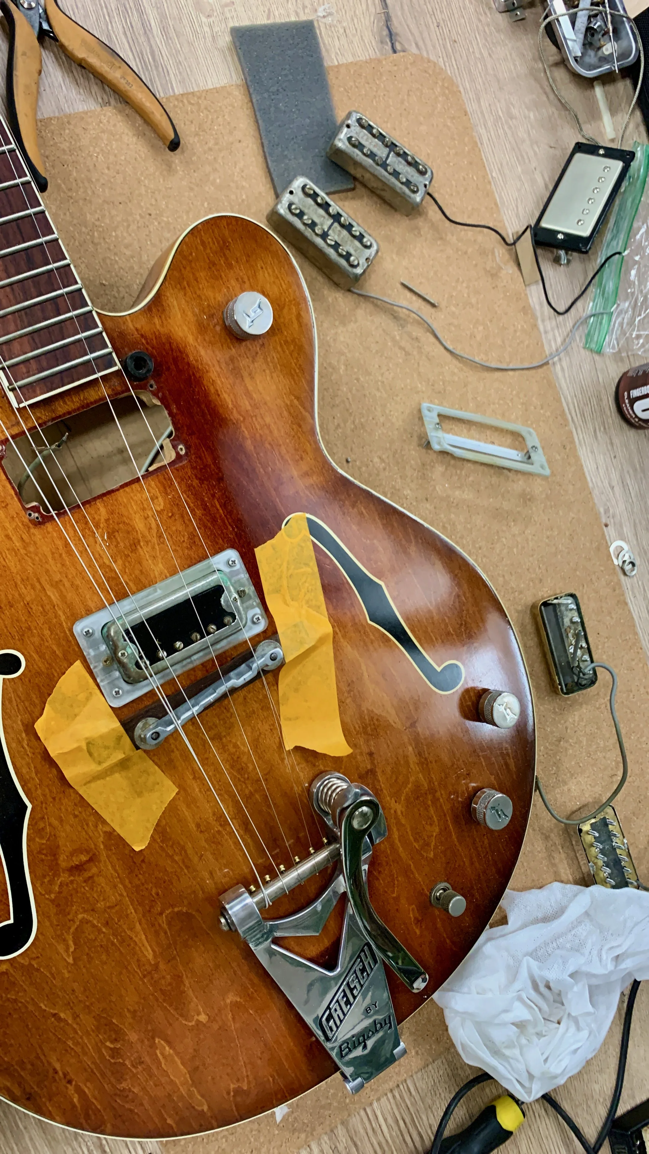 Een elektrische gitaar in reparatie met onderdelen en gereedschap eromheen.