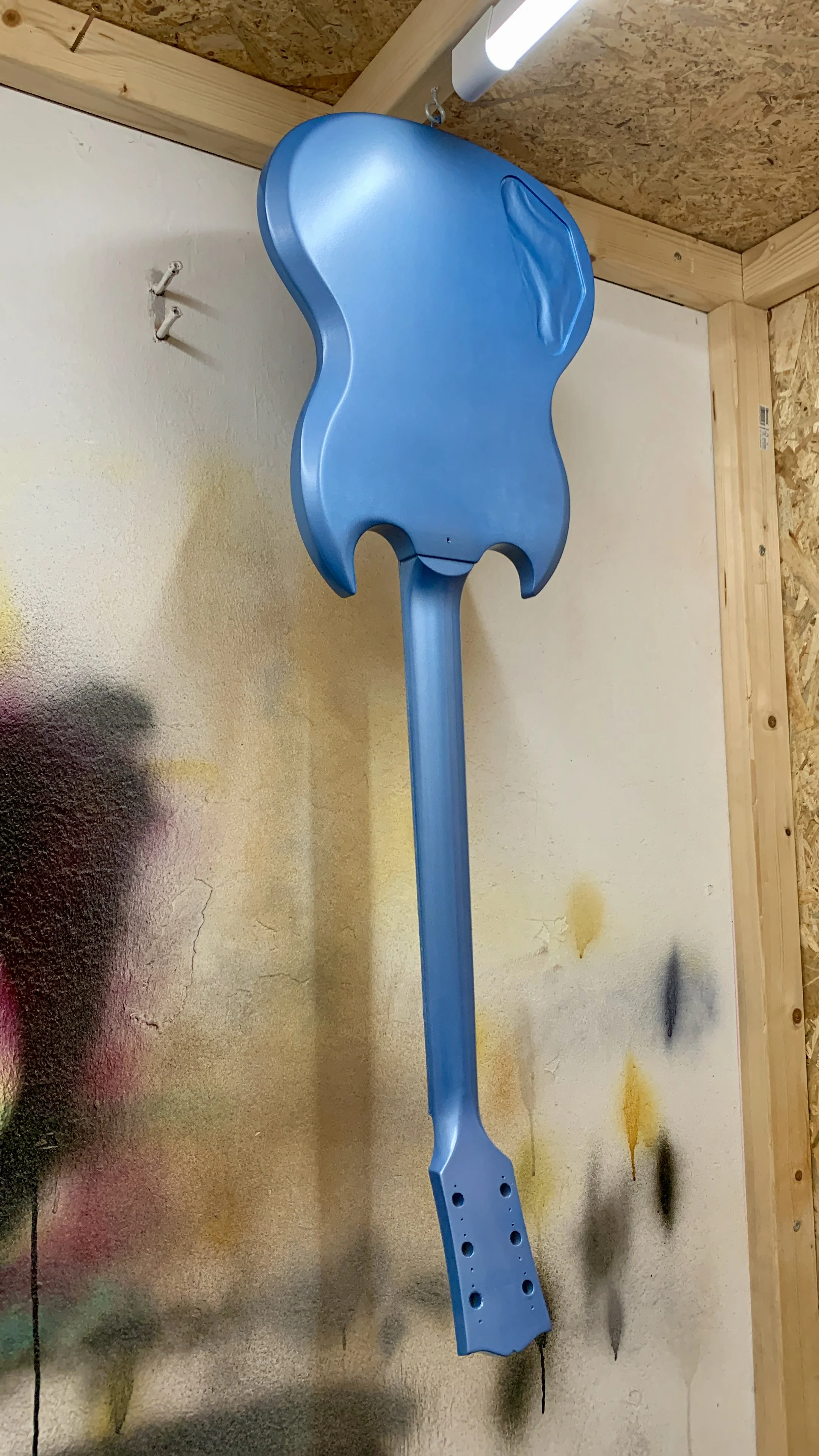 Een blauw metalen gereedschap dat lijkt op een spade, blijft hangen aan een lichtbron in een houten constructie.