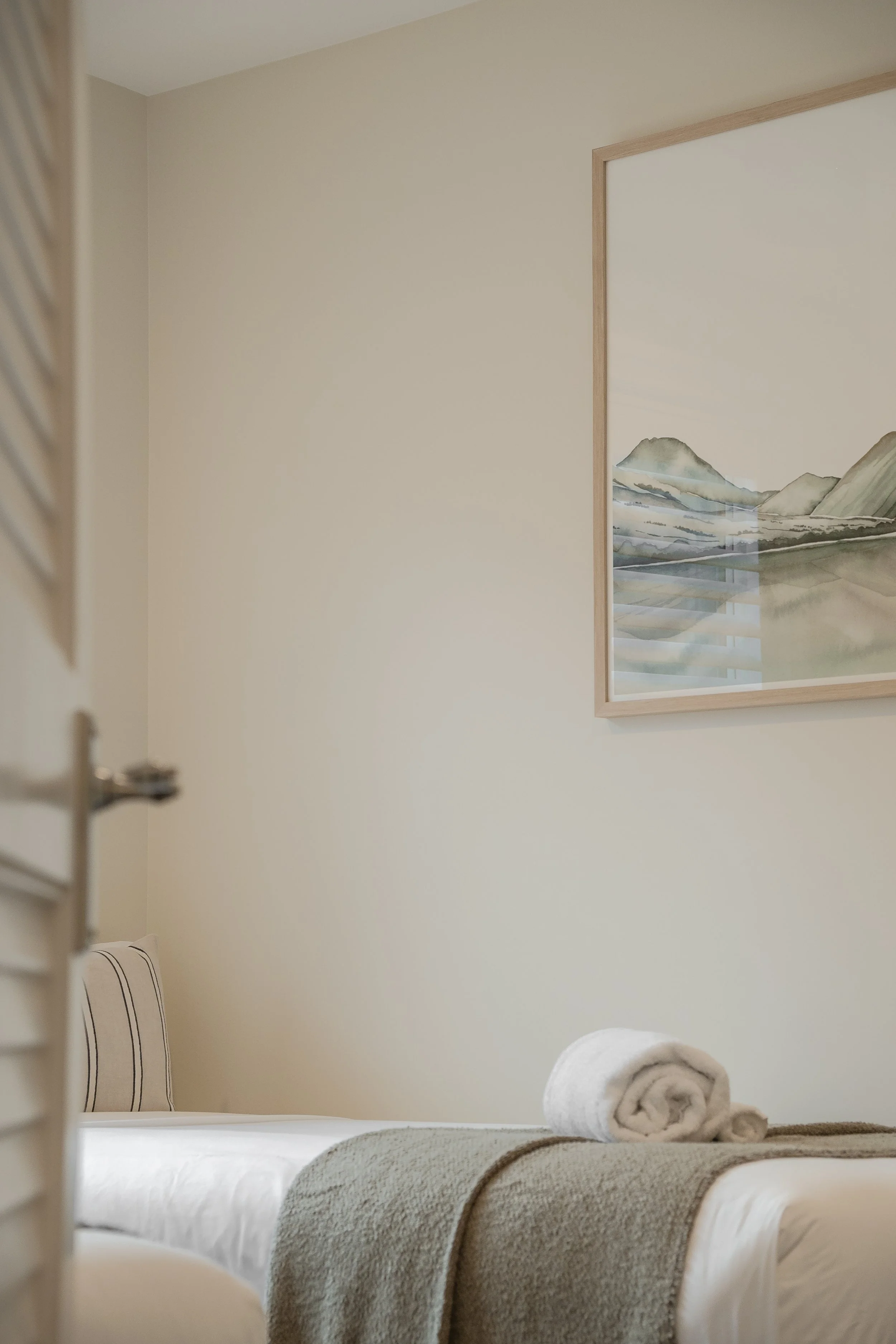 Peaceful Airbnb guest bedroom in Queenstown with soft bedding, rolled towel, and alpine artwork