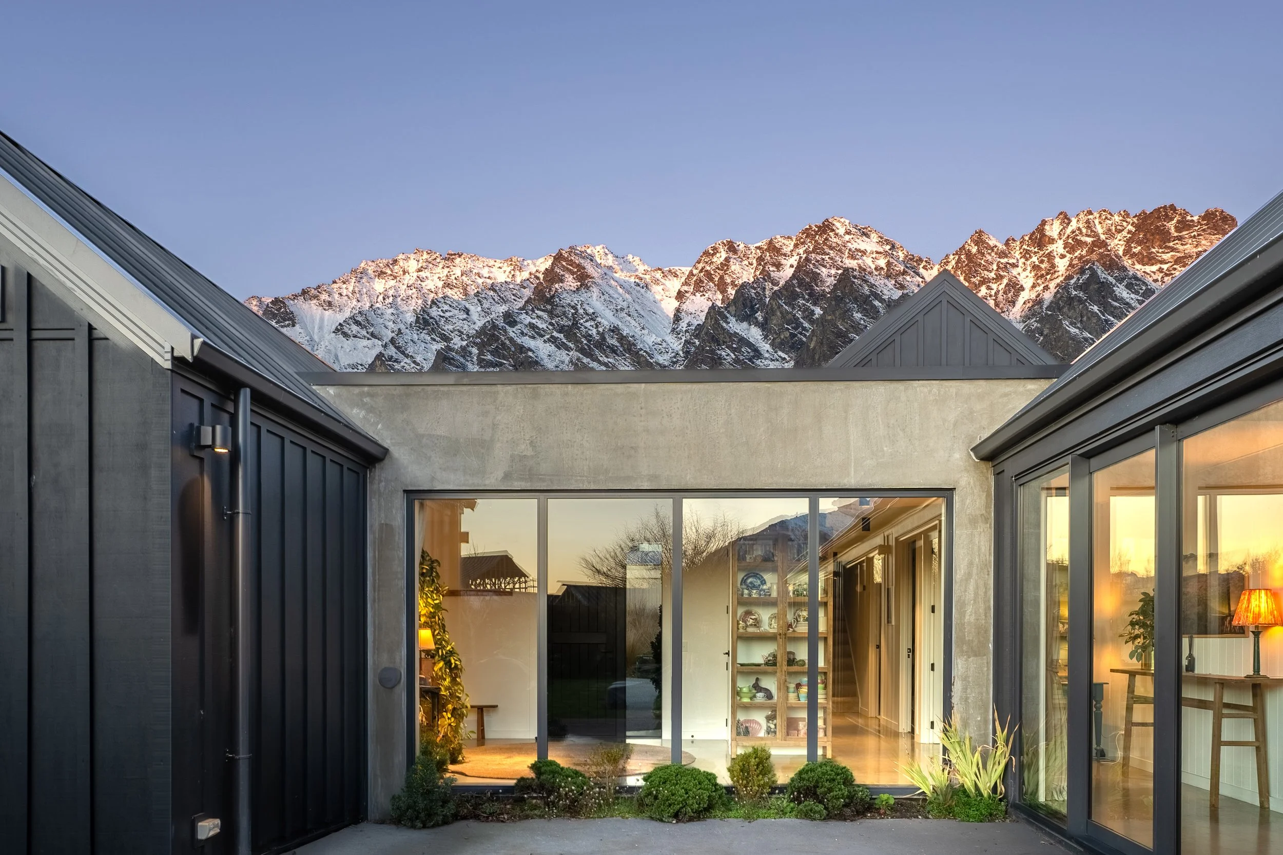 A modern mountain home glowing at golden hour. Clean lines, generous glazing, and the Remarkables rising behind it – a strong example of how light, design, and setting elevate a listing.