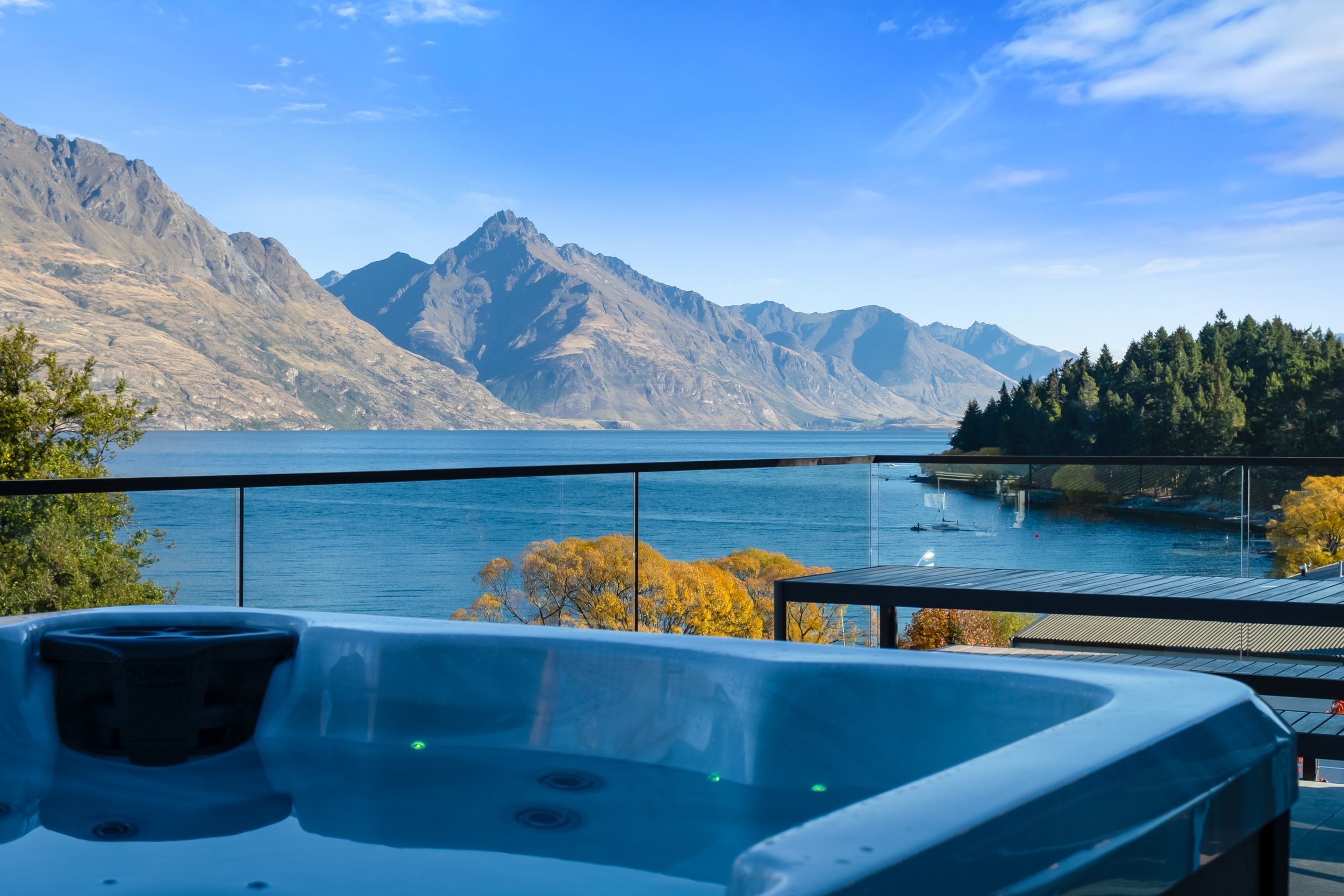 View of a scenic lake with mountain ranges in the background, taken from a balcony with a hot tub in the foreground.