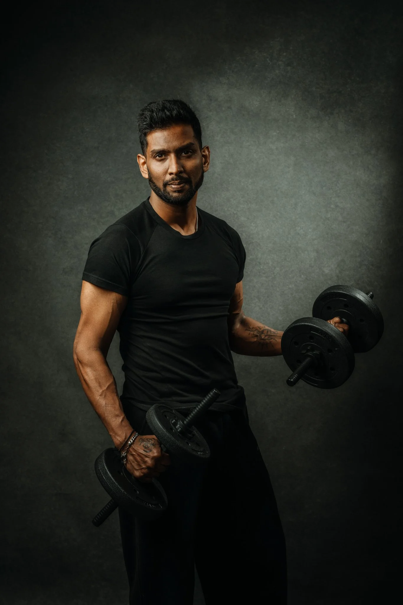 A man lifting dumbbells in a dark, plain background.
