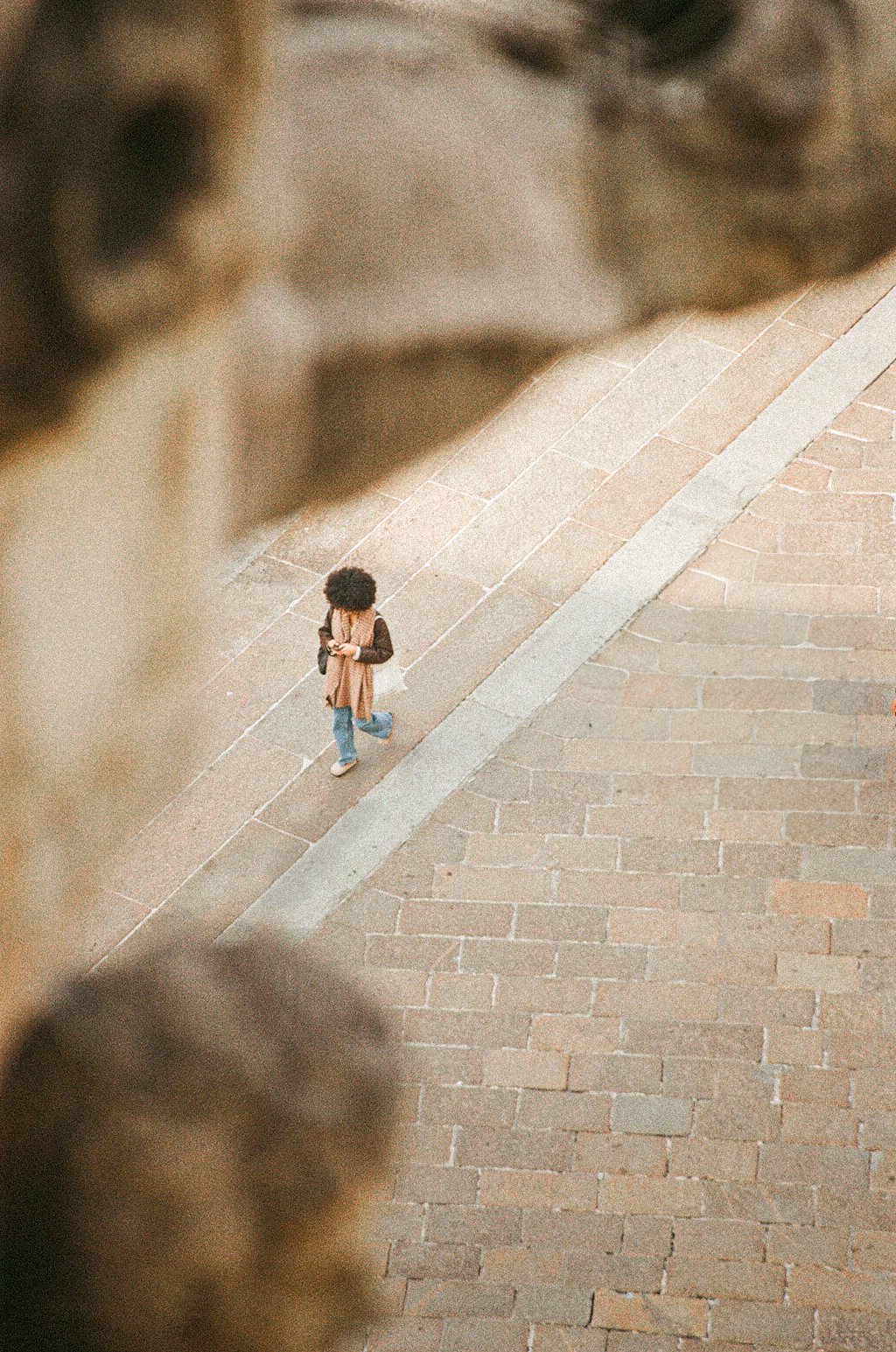 A woman with curly hair walking on a brick sidewalk, seen from an elevated perspective.