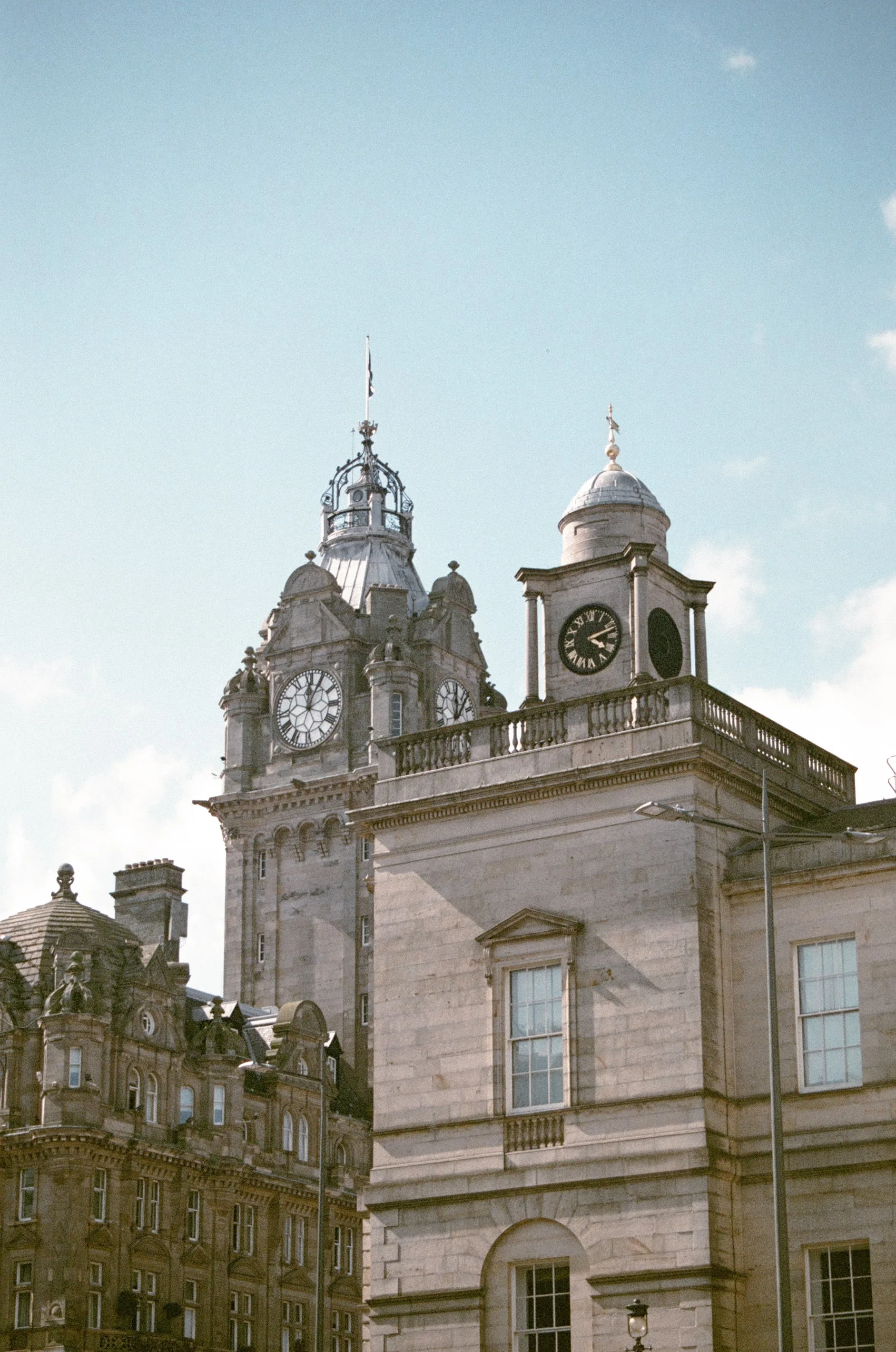 View of historic European-style building with clock towers and ornate architecture in Edinburgh, against a blue sky with a few clouds.