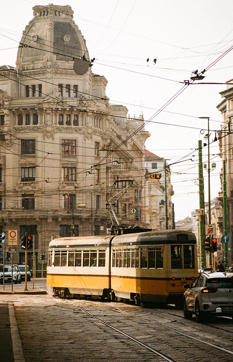Milanese street scene with a vintage tram, multiple overhead power lines, and tall historic buildings in the background during daytime.