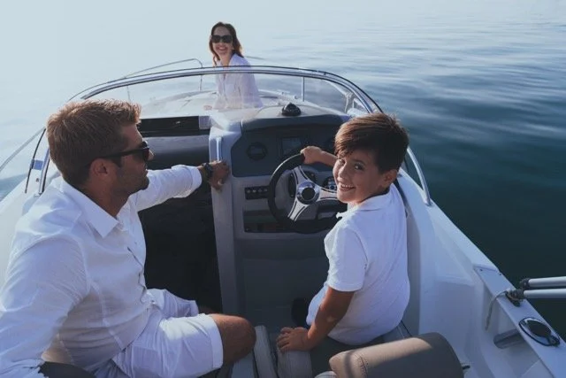 A family enjoying a boat ride on the water, with a woman in the background smiling at the camera.