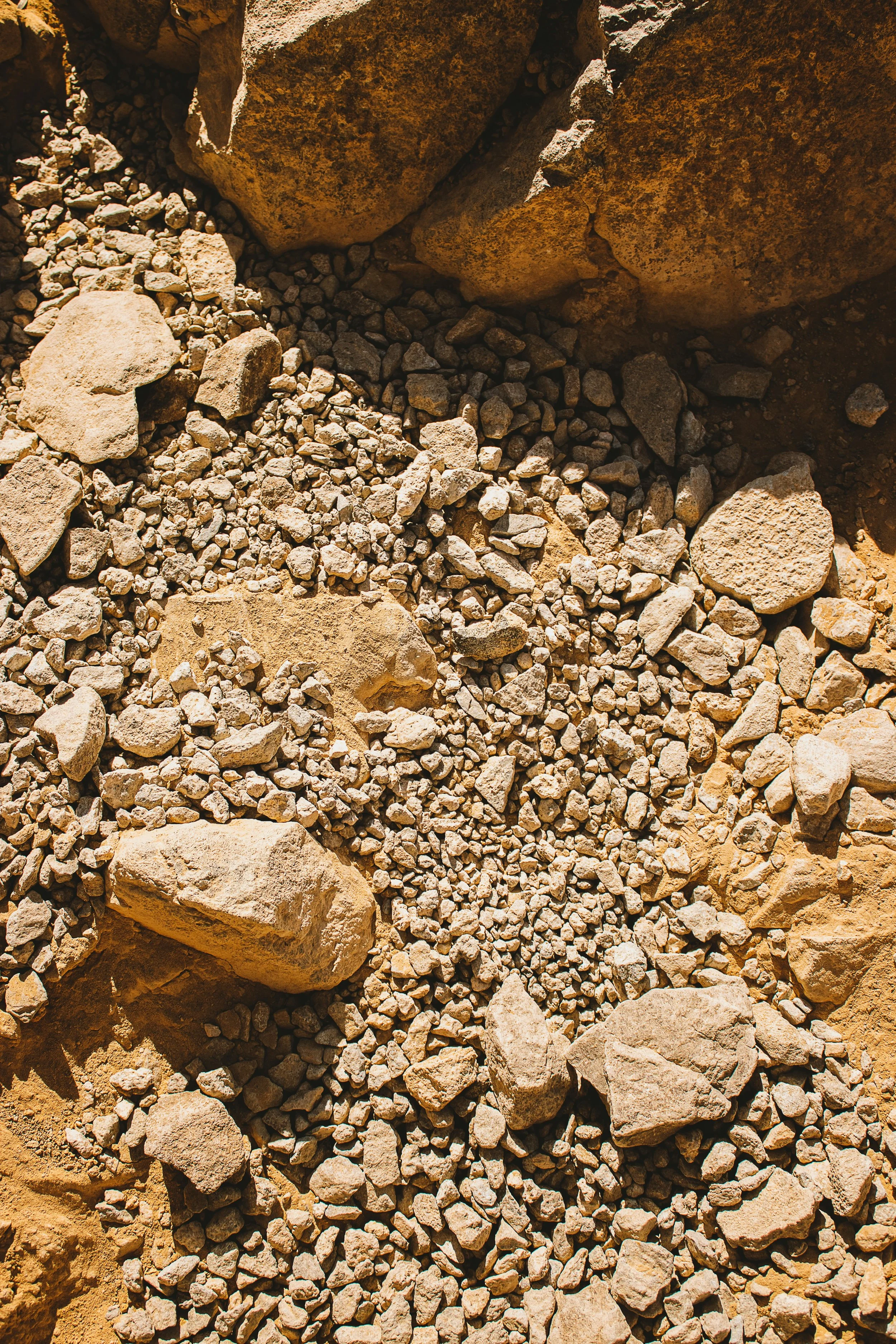 Close-up of a rocky, sandy terrain with small and large rocks scattered, some partially embedded in the ground.