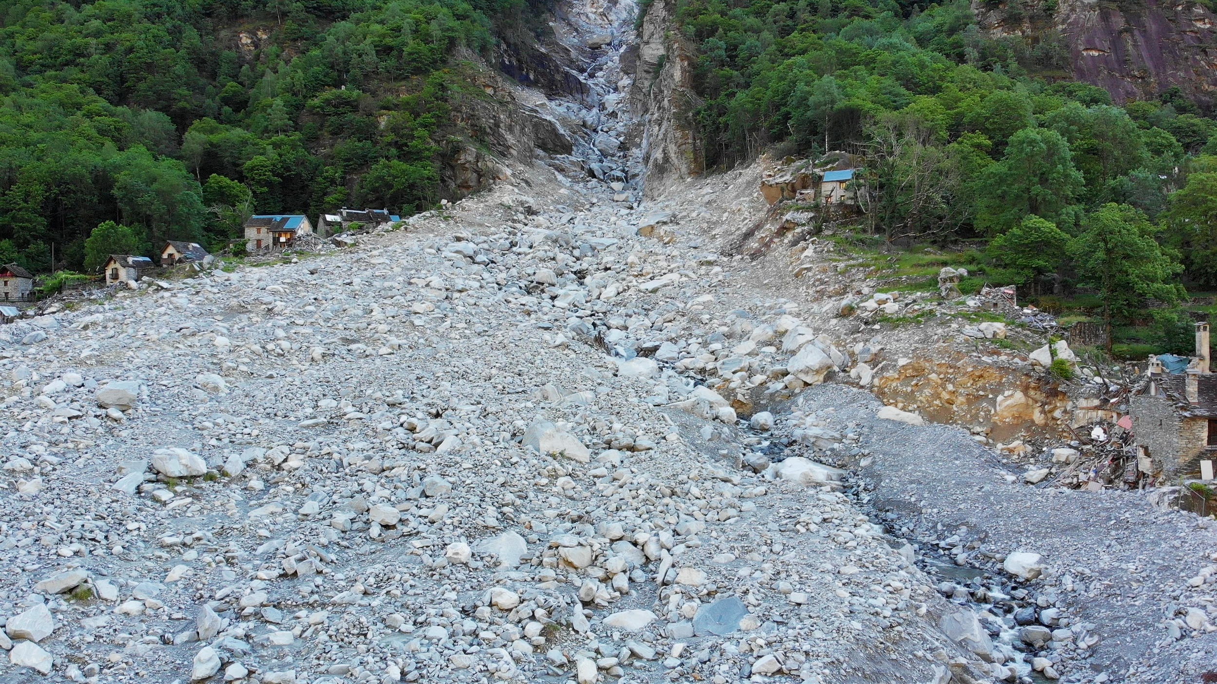 Erdrutsch in einer bergigen Gegend mit einigen Häusern und viel Gestein und Geröll