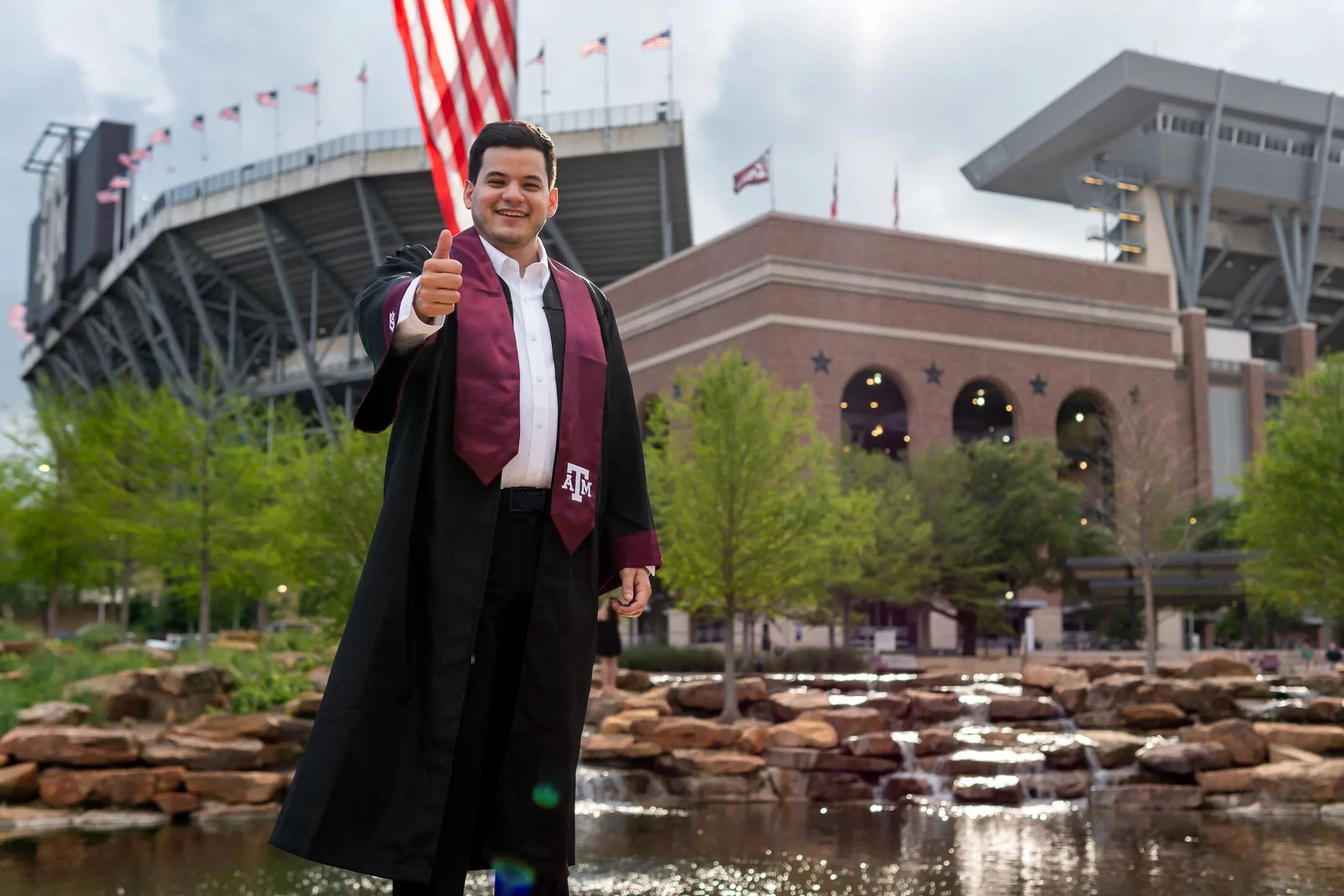 An A&M graduate posing with Kyle Field behind to be captured by a photographer for graduation.