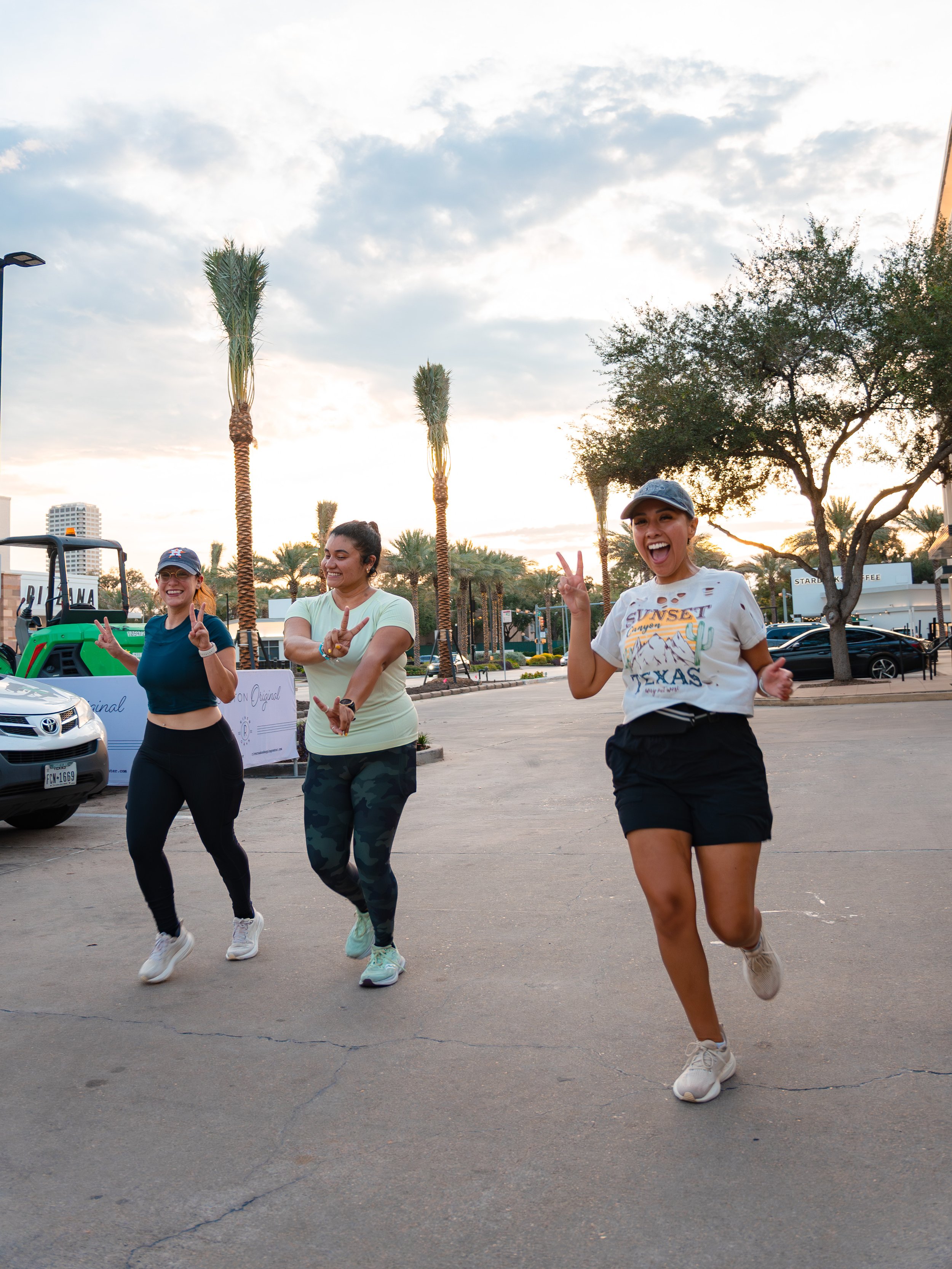 Three women cheerfully running outdoors in a parking lot, posing for a Houston Photographer to capture them.