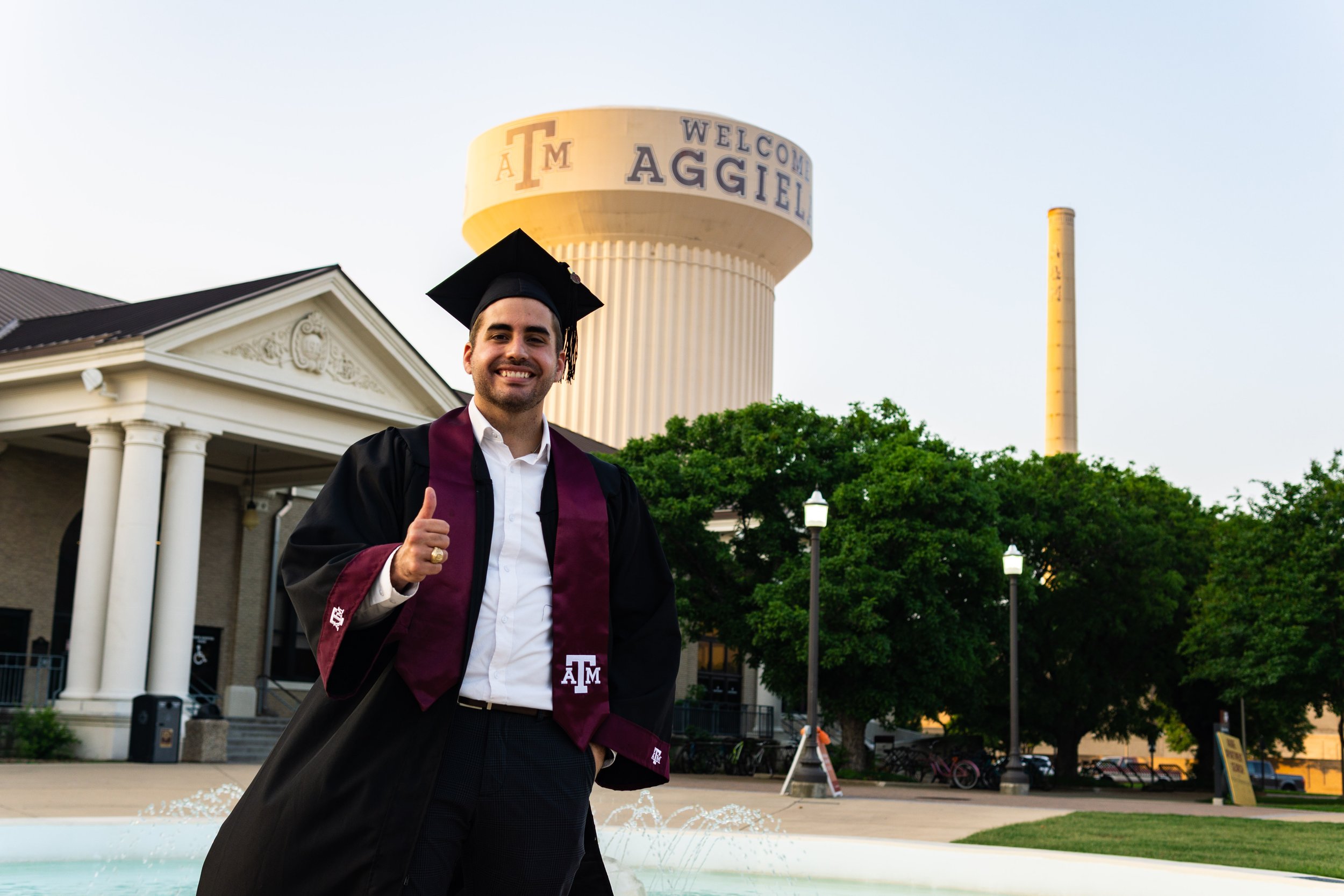 An aggie posing with the A & M water tower for his graduation pictures, by a graduation photographer.