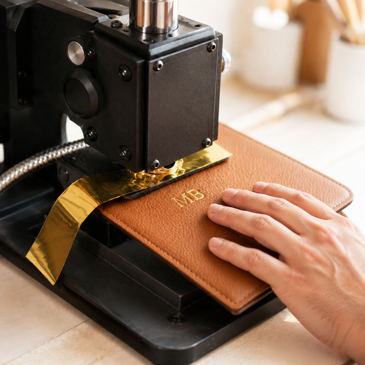 Personalized leather item being monogrammed with gold foil on a professional embossing press