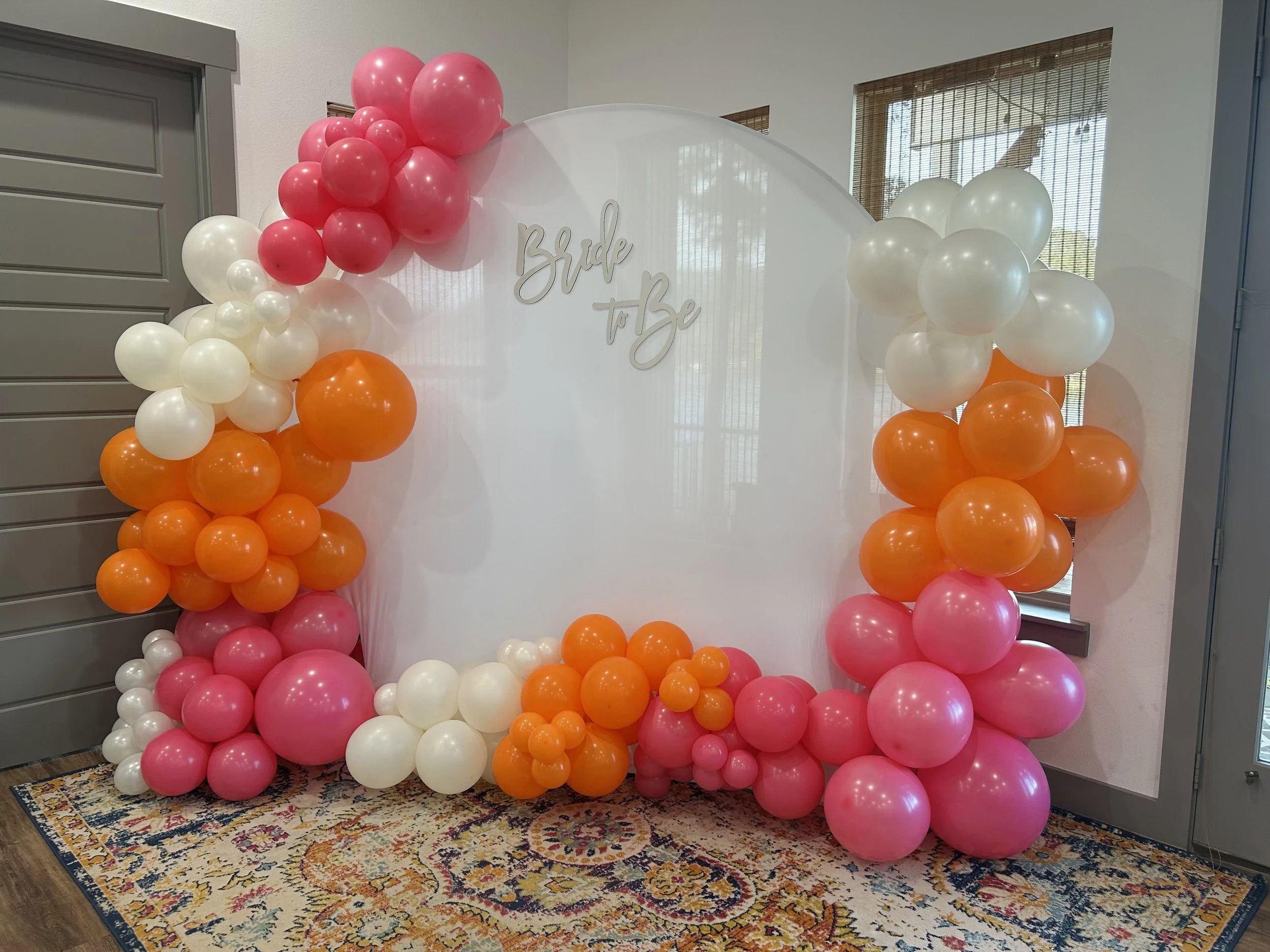 Balloon arch decorated with pink, orange, and white balloons, featuring Bride To Be White Cloth Backdrop set up in a home interior, perfect for photo ops.