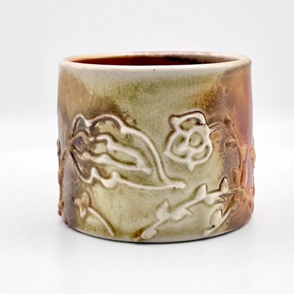 Cream-colored ceramic cup with embossed floral design on white background.