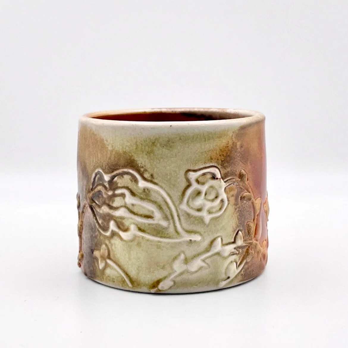 A ceramic mug with a floral embossing design, filled with a dark beverage, against a plain white background.
