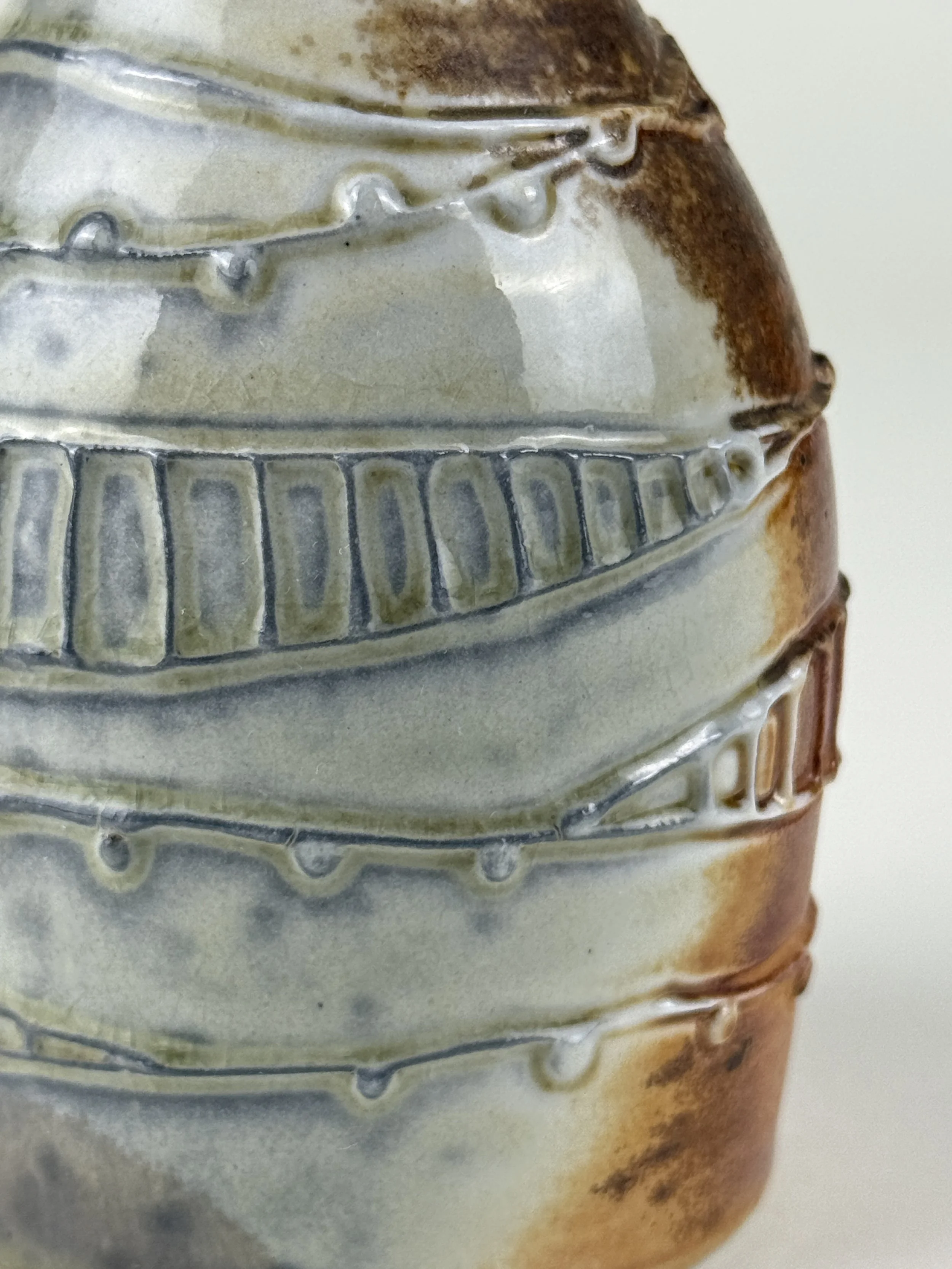 Close-up of a layered ceramic pottery piece with textured patterns and a mix of cream, brown, and gray colors.